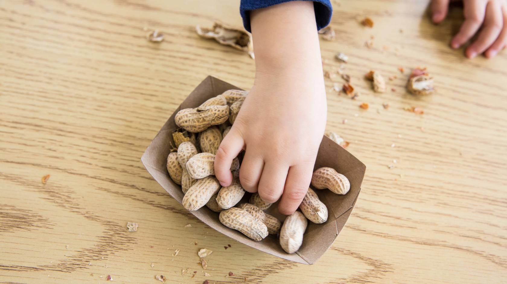 A child's hand reaching for peanuts