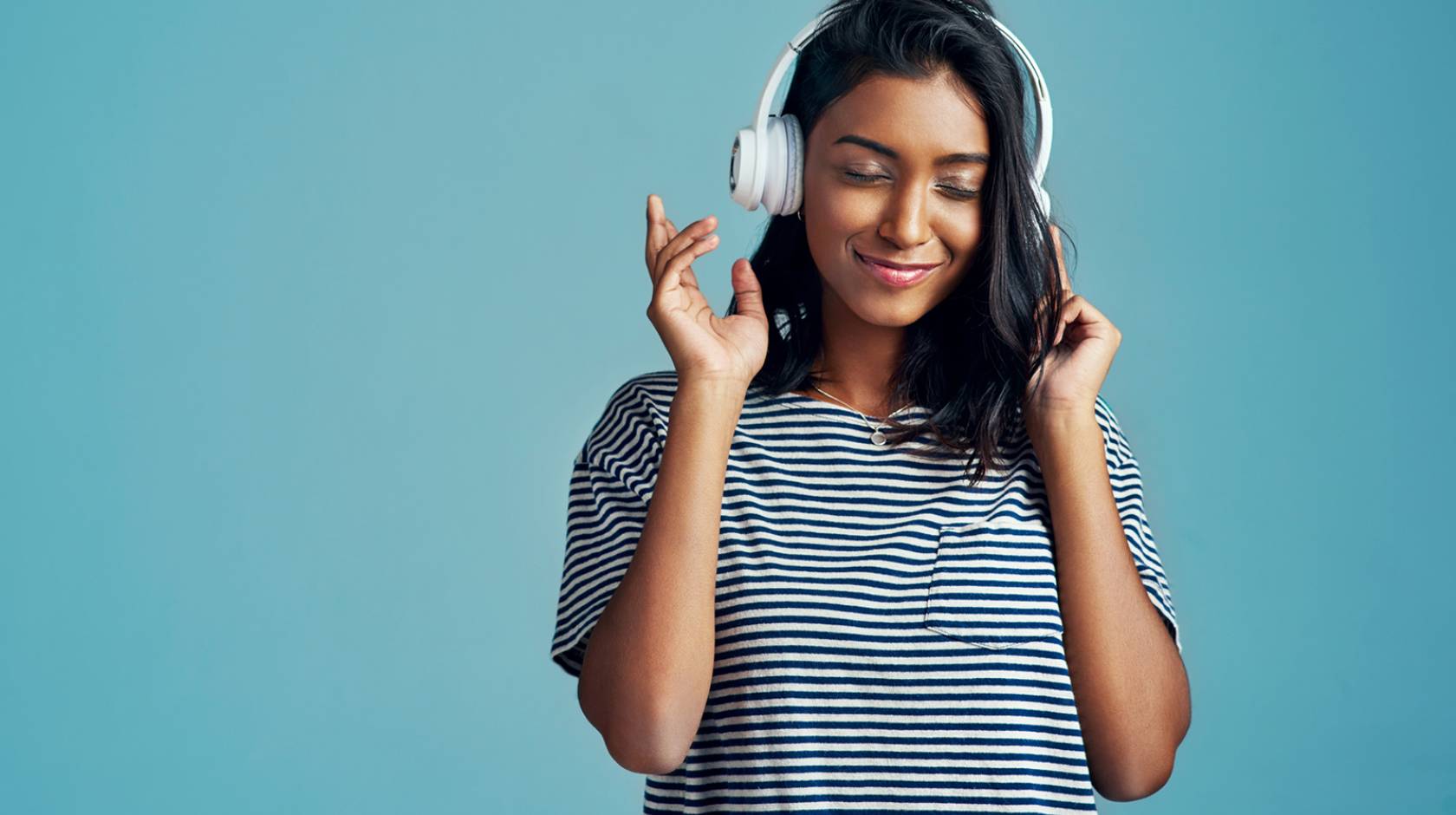 Young South Asian woman listening to headphones smiling and pointing finger