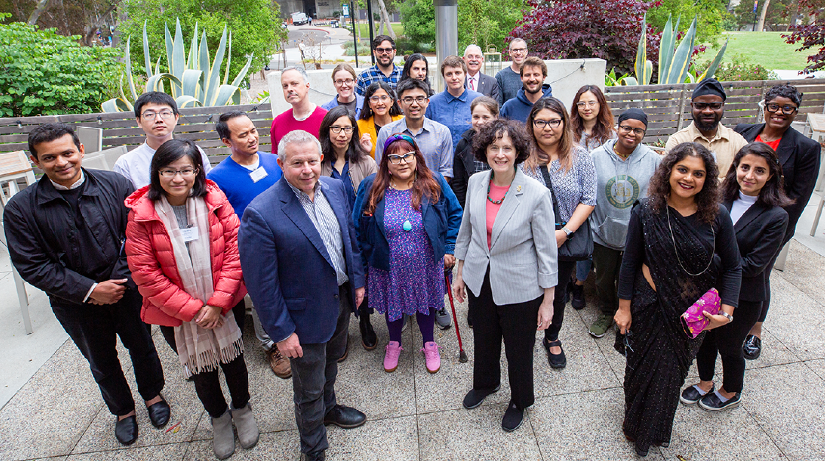 A group of people stand on a patio with lots of plants smiling for a group photo