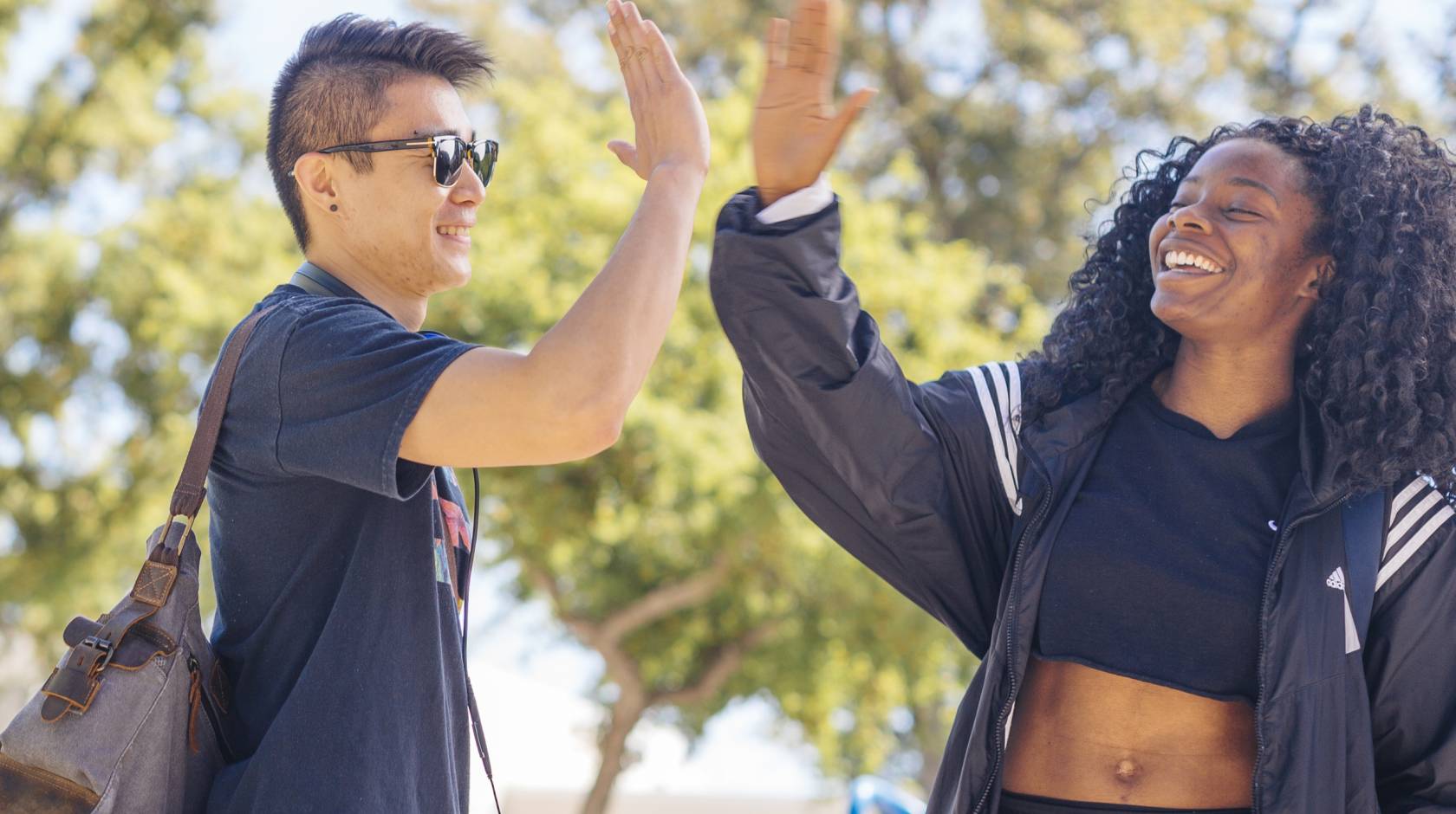 Two UC Davis students, a young Asian man and young Black woman, give each other a high five