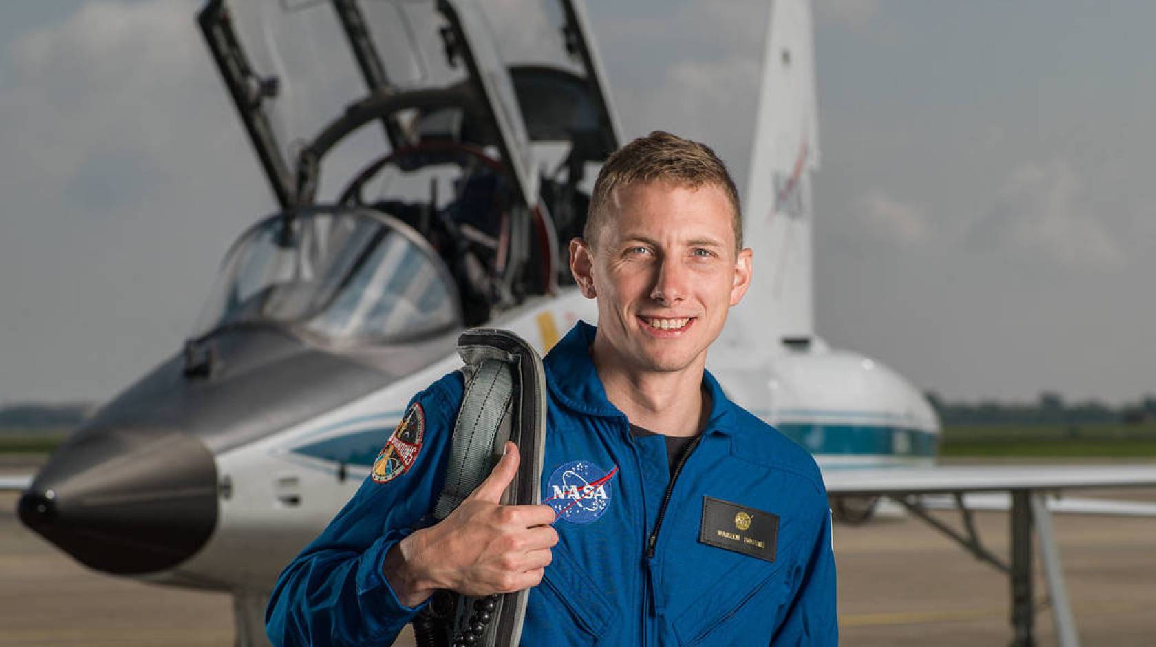 Warren Hoburg in blue spacesuit in front of an aircraft