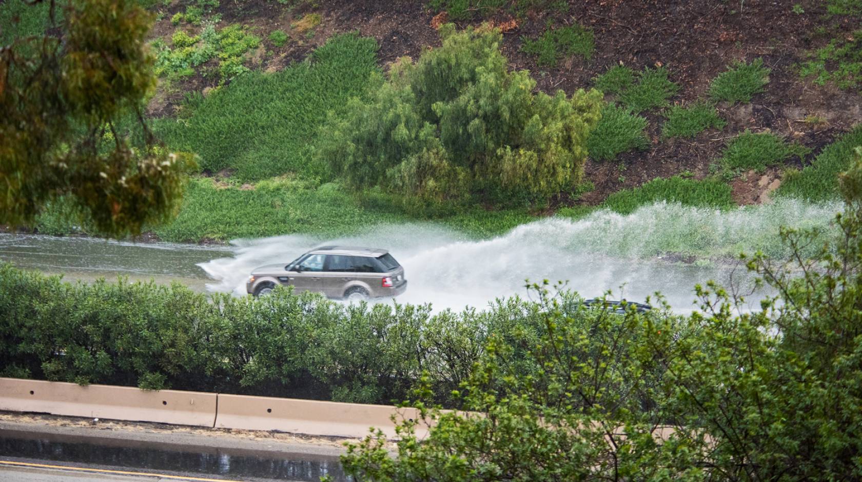 SUV driving a flooded freeway, water splashing behind