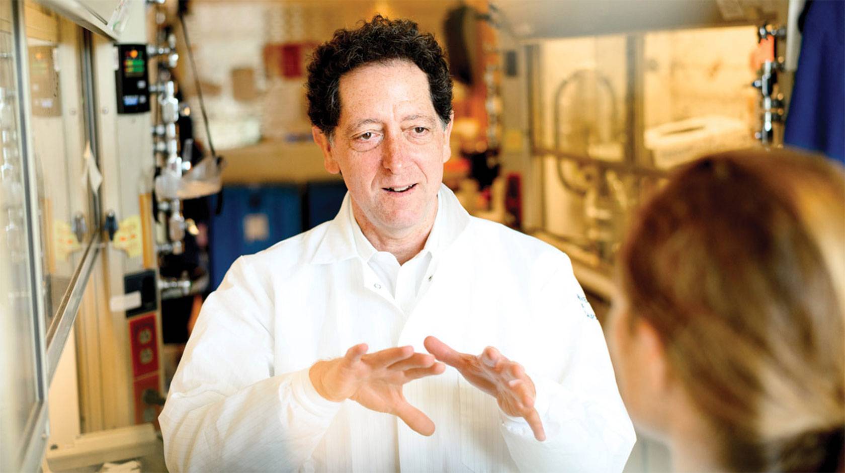 Kevan Shokat in a white lab coat speaking to a grad student in a lab.