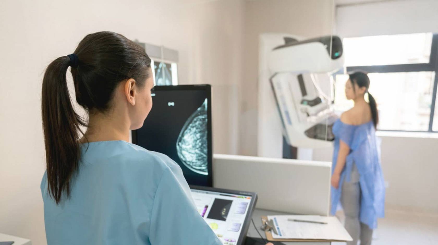 Nurse and patient conducting a mammogram, patient in front of machine