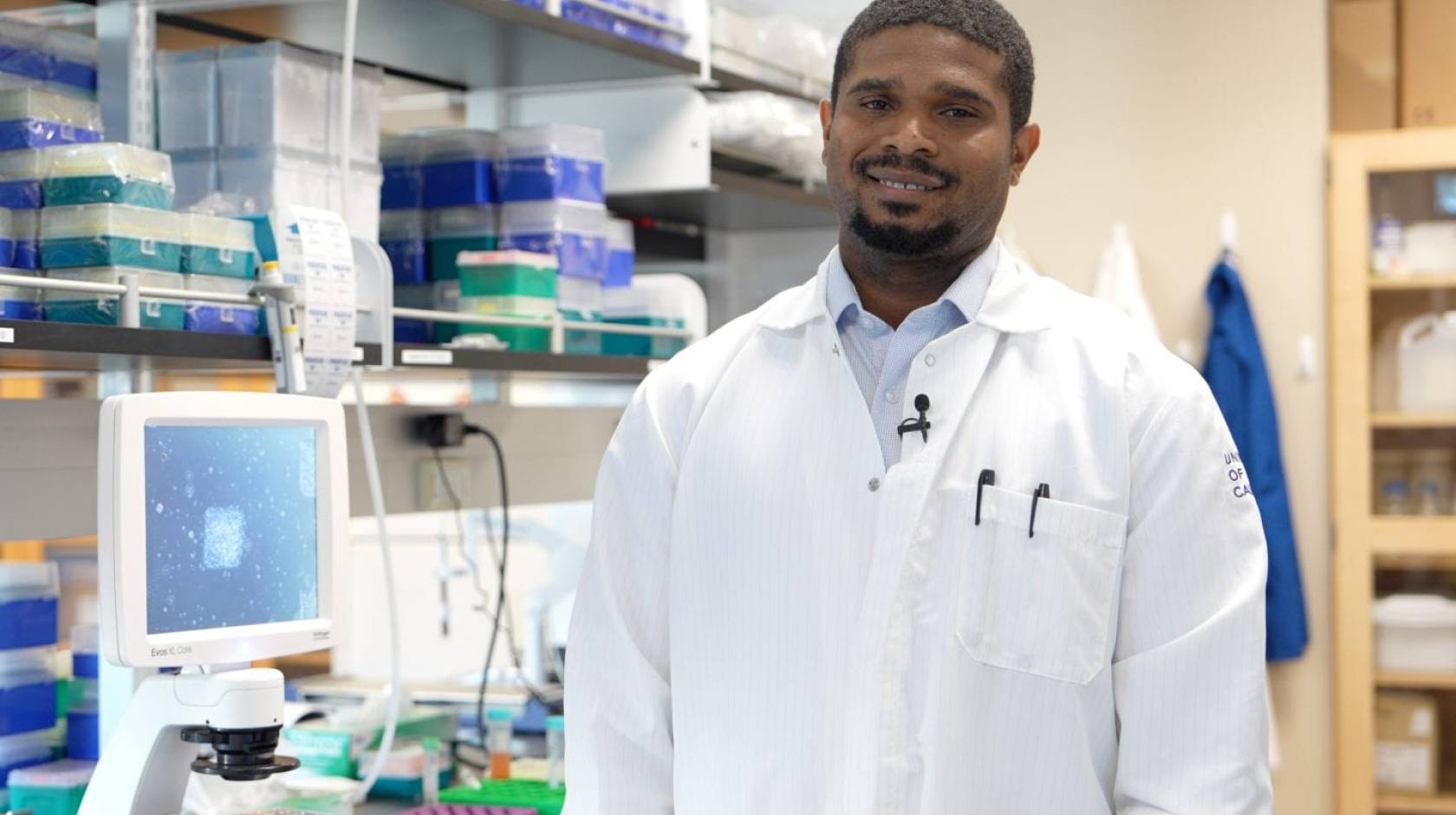 Young Black man with a goatee in a lab coat in a lab, smiling