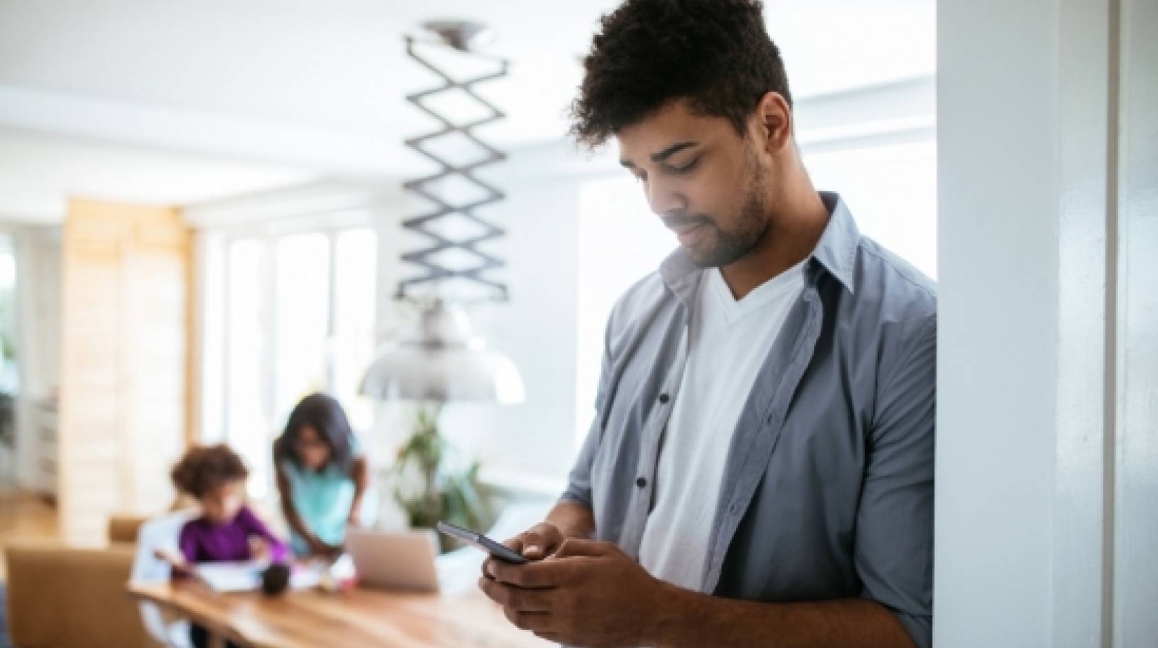 A man uses a smartphone while his kids are at a table in the background