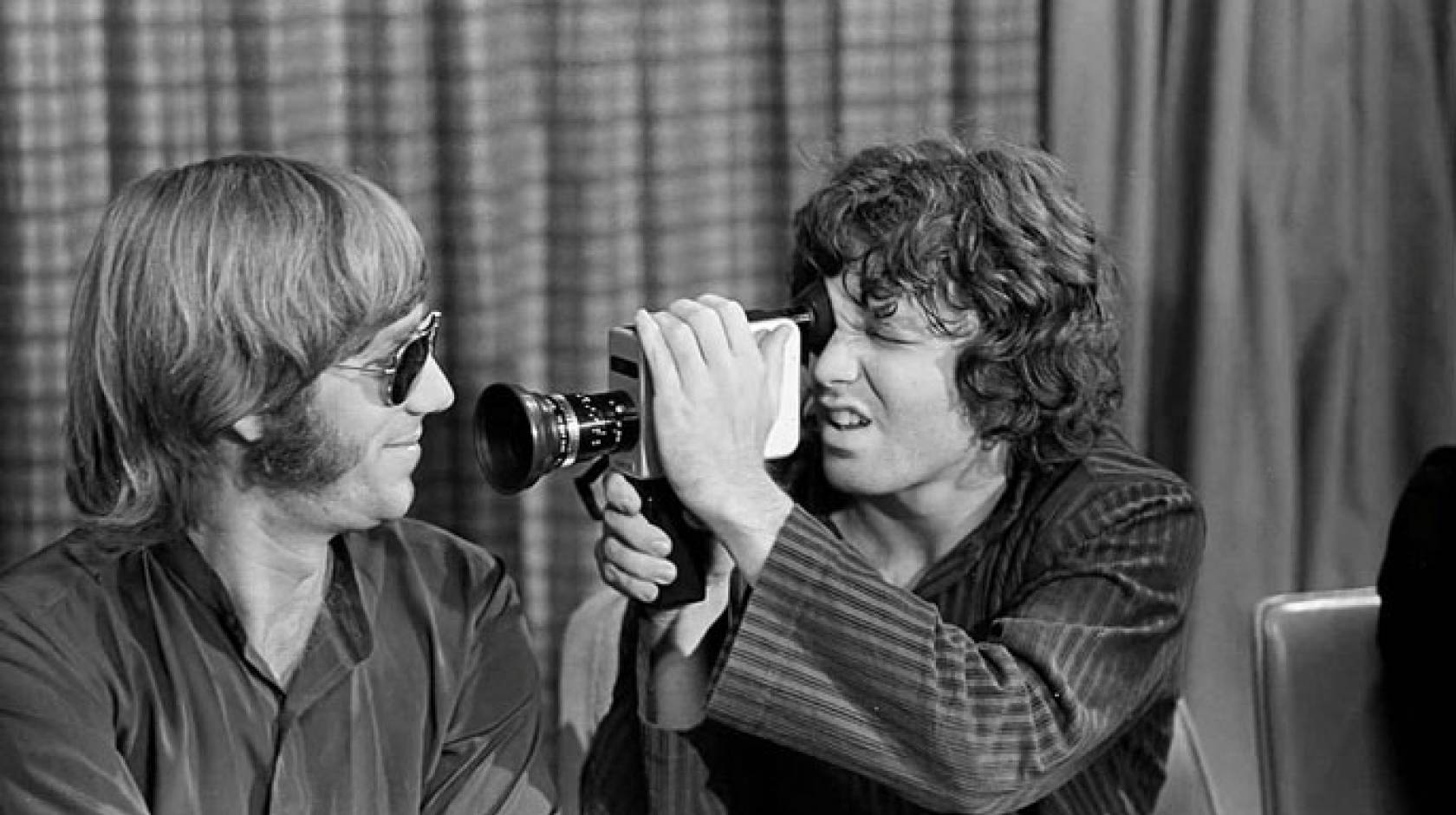 Jim Morrison holding a film camera up to Ray Manzarek
