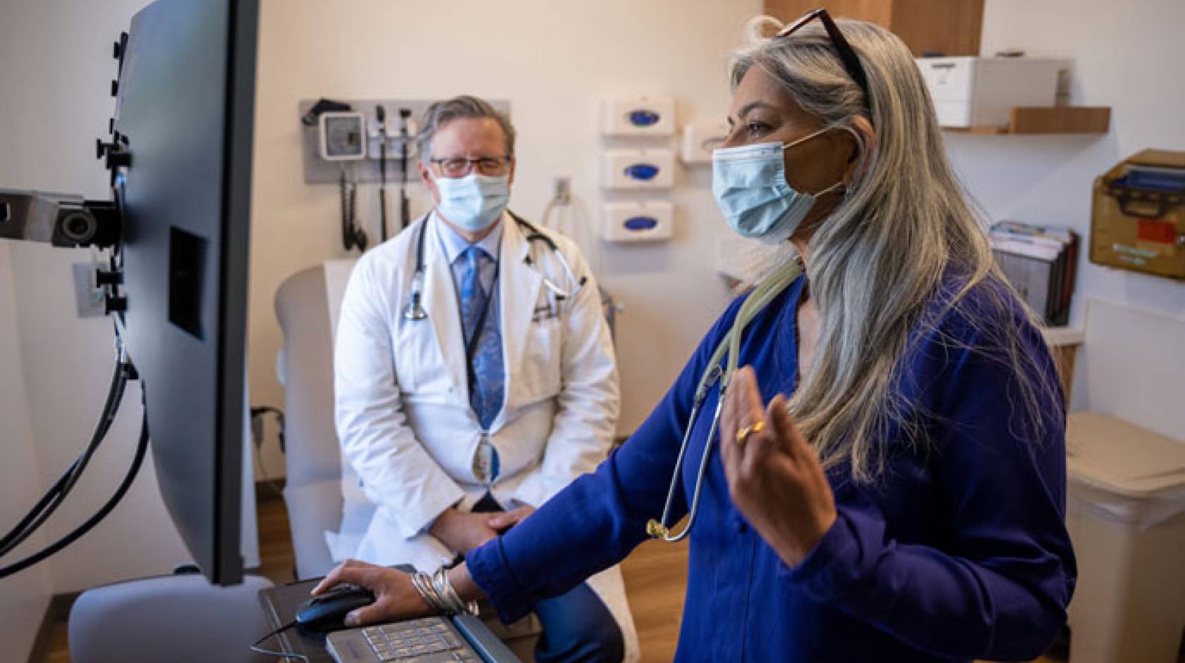 Two medical professionals in an office, one looking at a screen