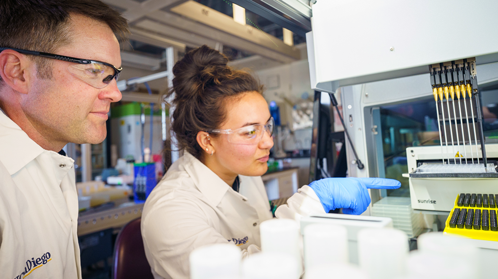 A man and a woman pointing at a machine in a lab