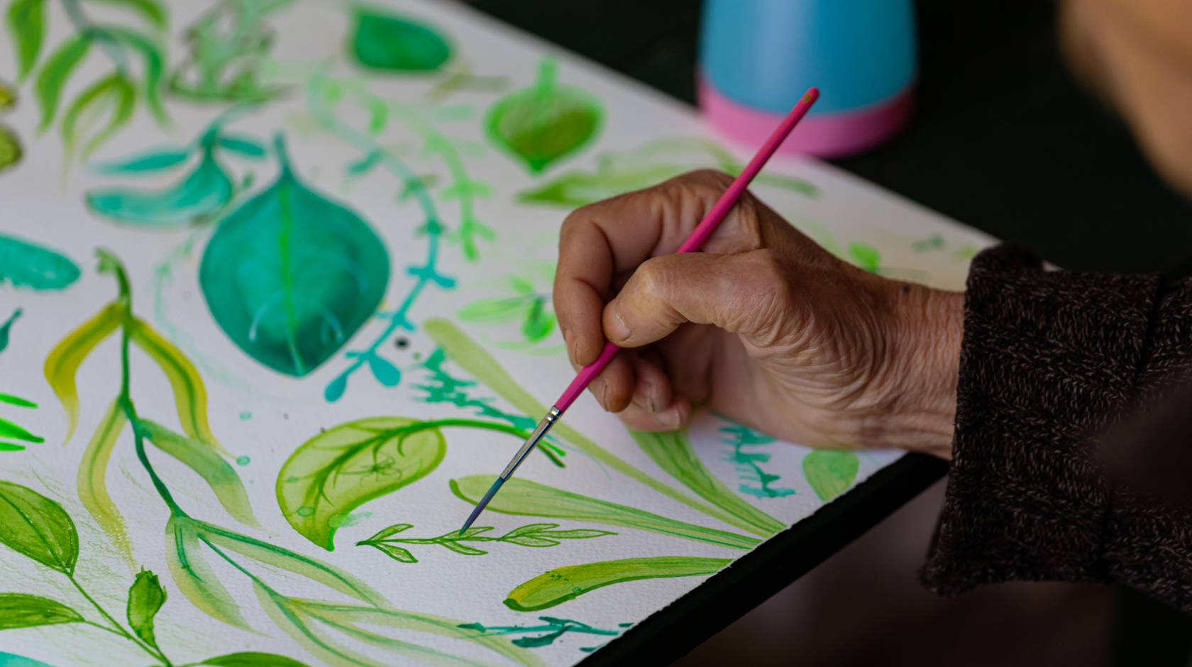 An older adult painting, hand on leaf decorative painting pictured