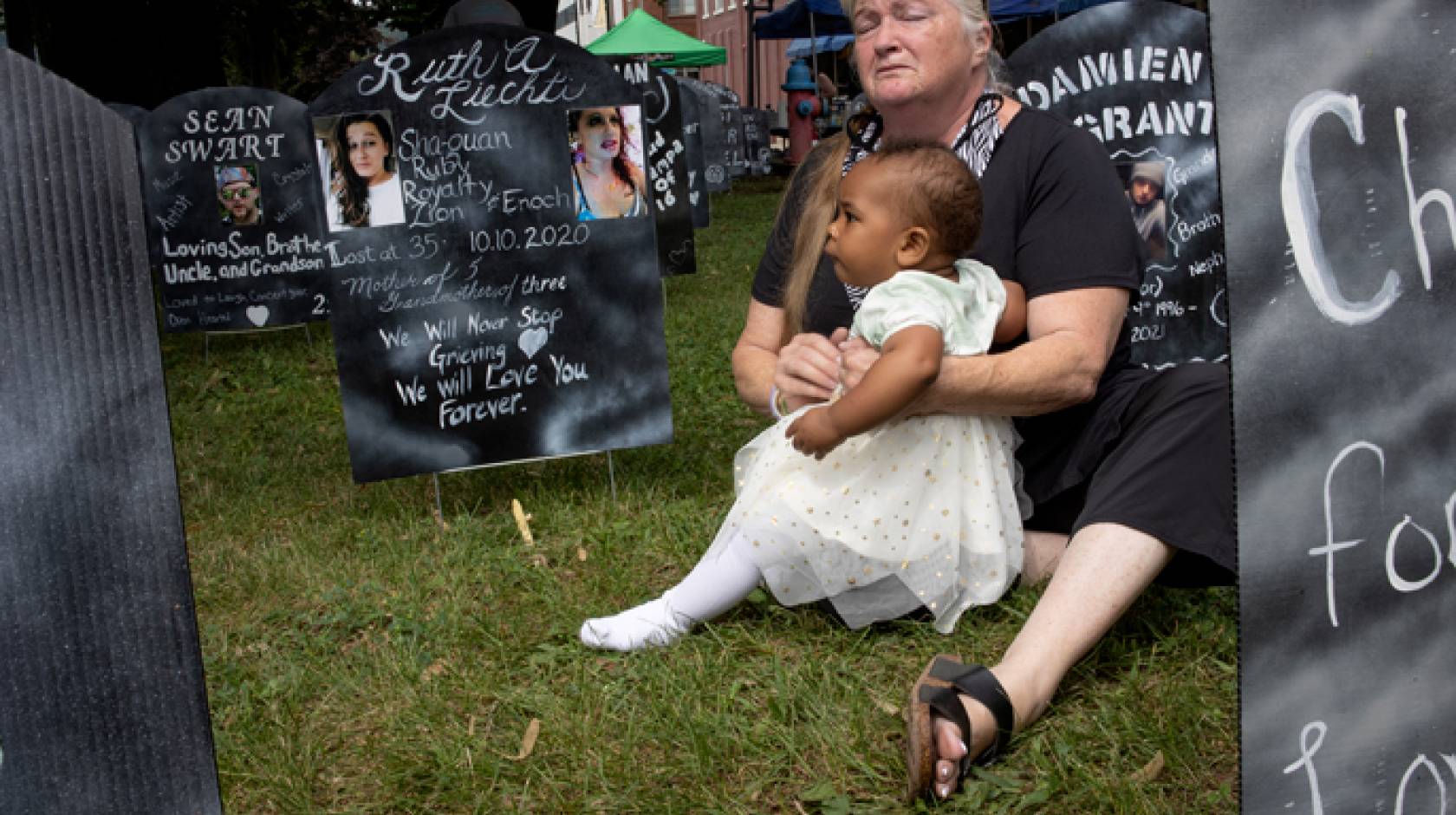 A woman holds a young child near an opiate memorial