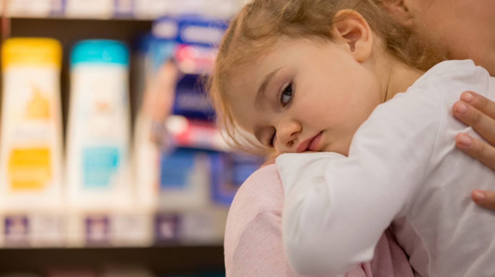 Child on parent's shoulder in front of personal care products