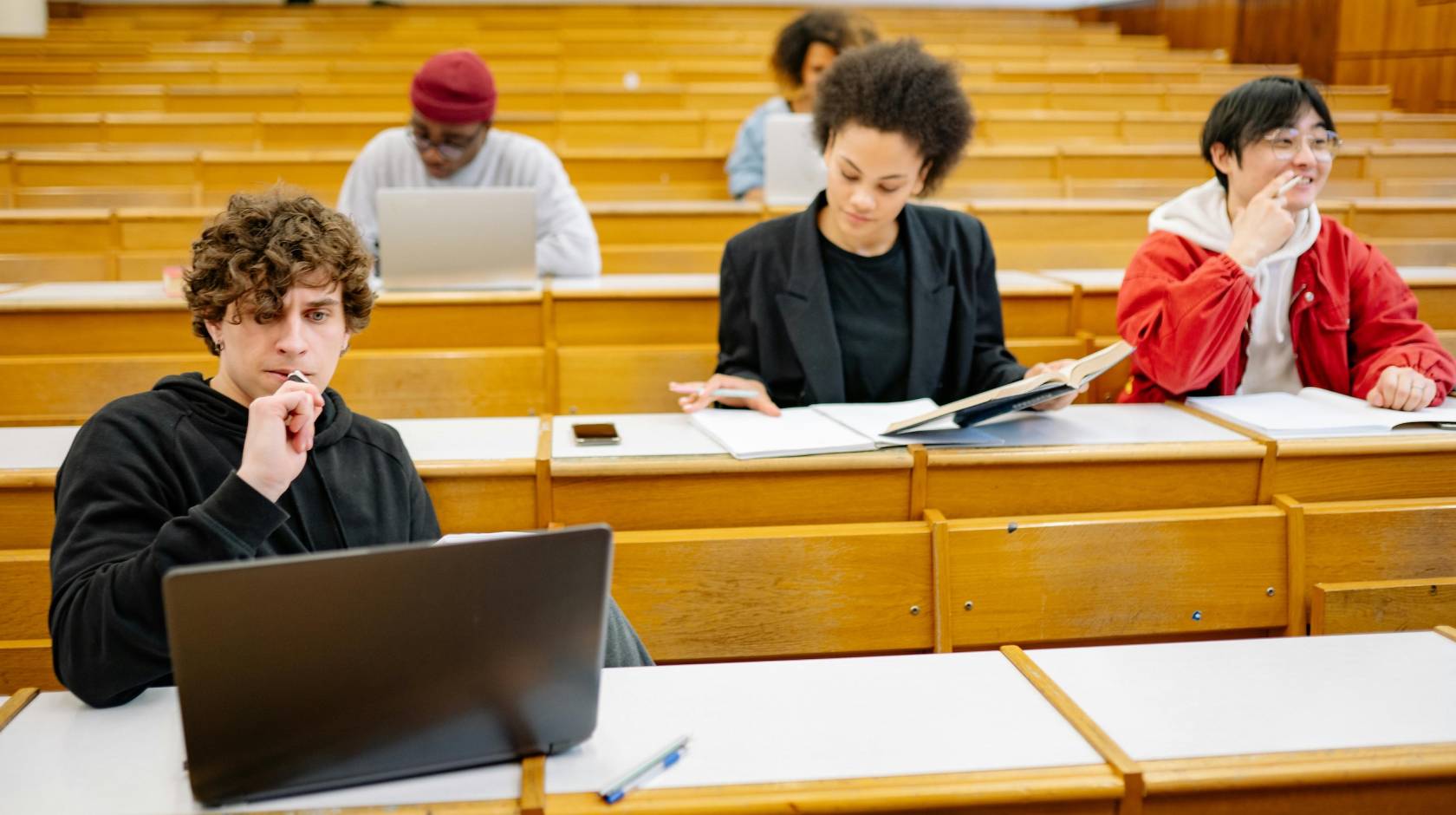 Five students in four rows of a lecture hall work independently