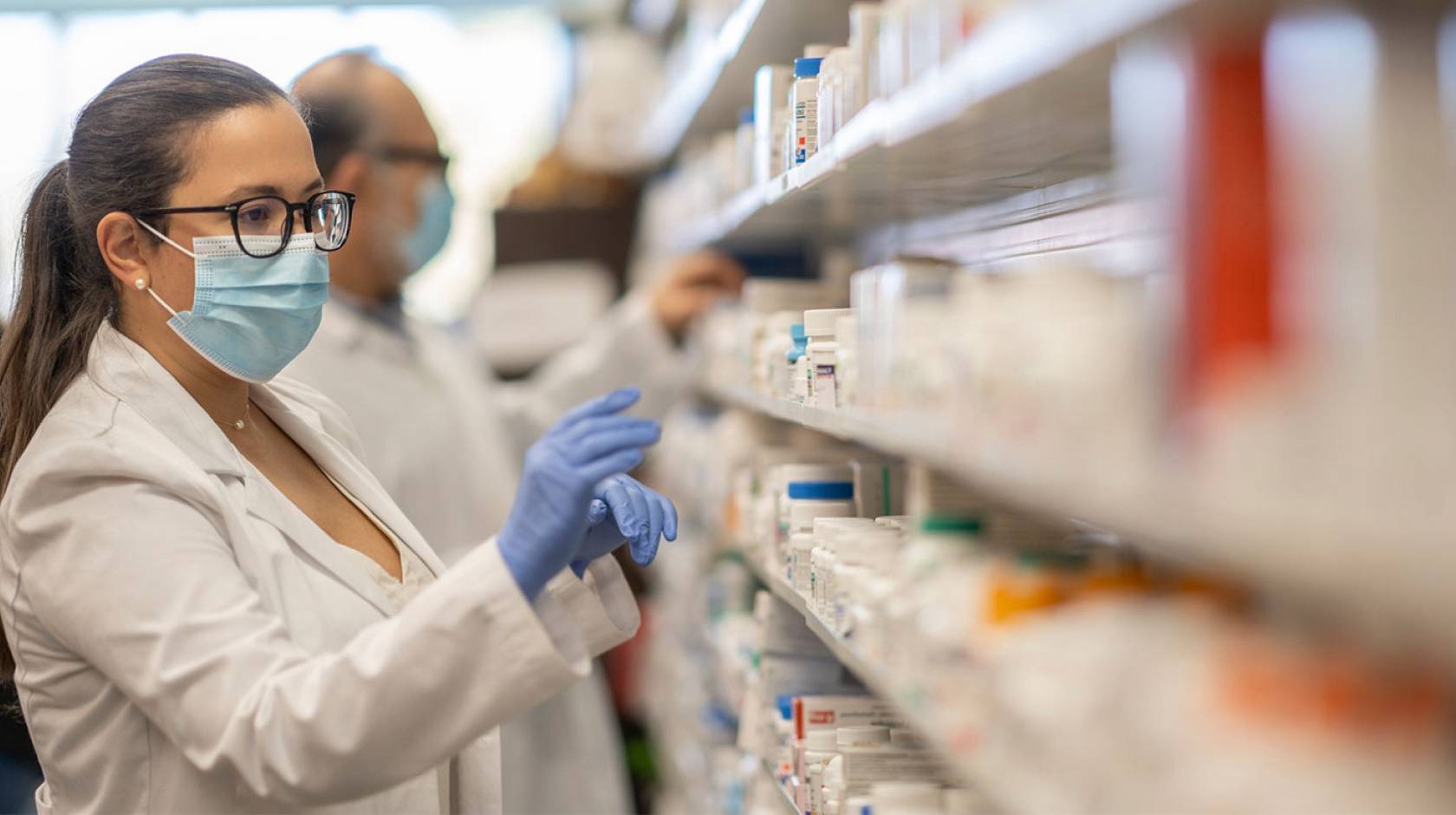 A pharmacist in a face mask reaching for drugs