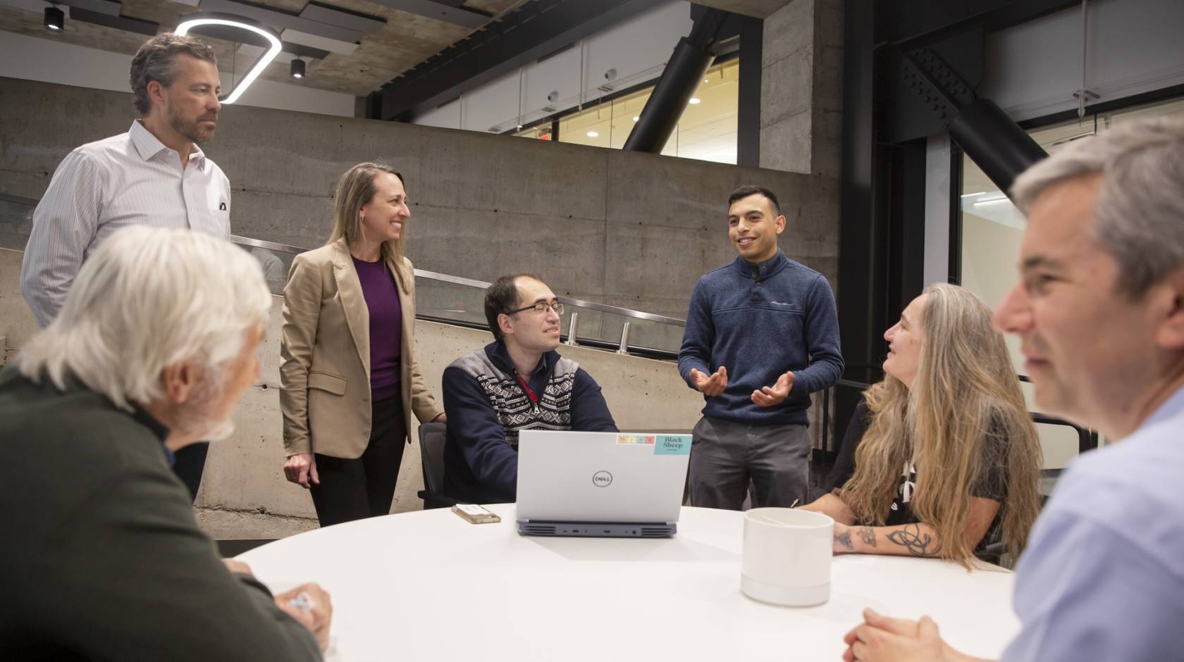 A group of people discussing, a few standing, while in an industrial or modern office space