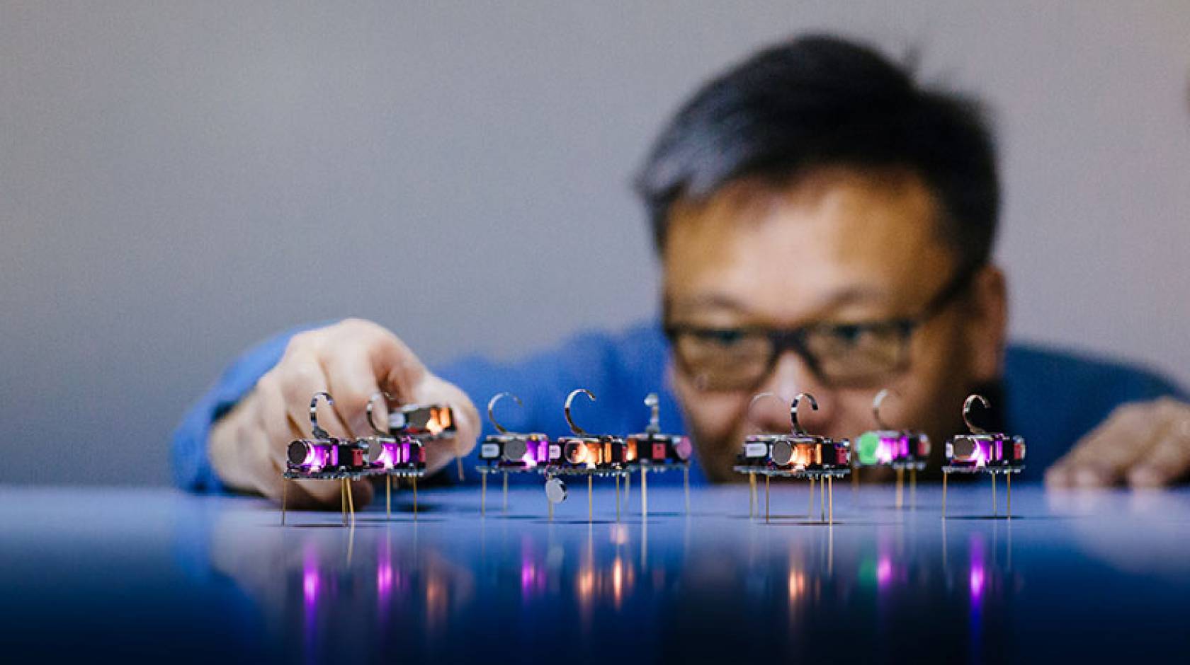 A researcher adjusts a row of small illuminated electronic devices on a reflective surface.