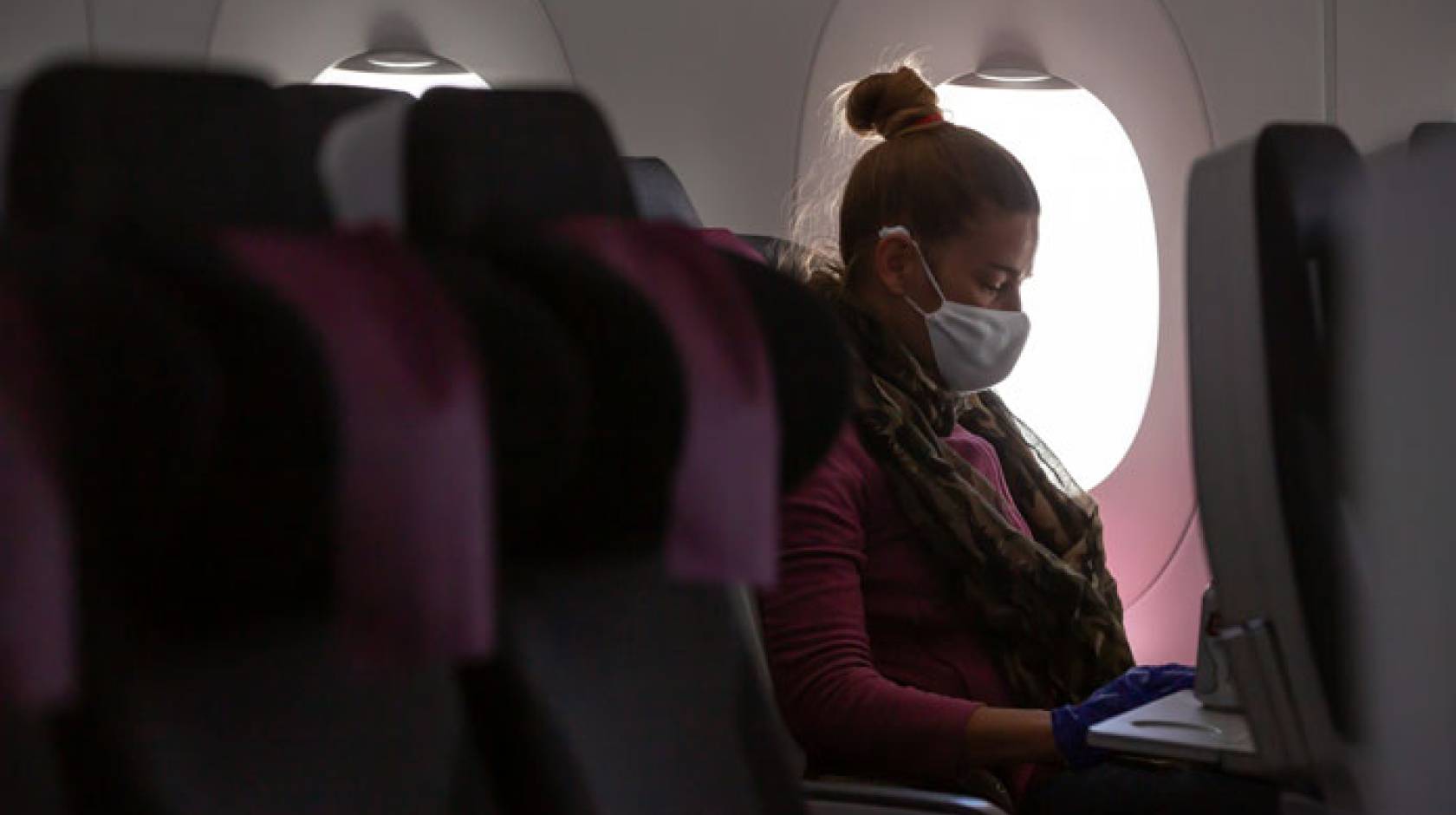 Woman on a plane wearing a mask alone in her row