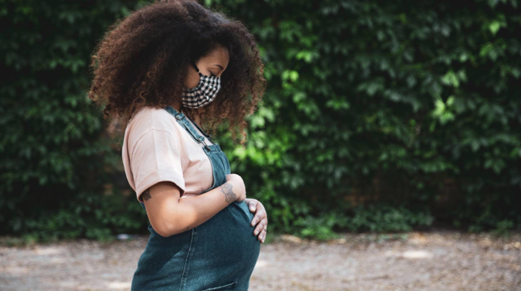 Black pregnant woman cradles stomach outdoors
