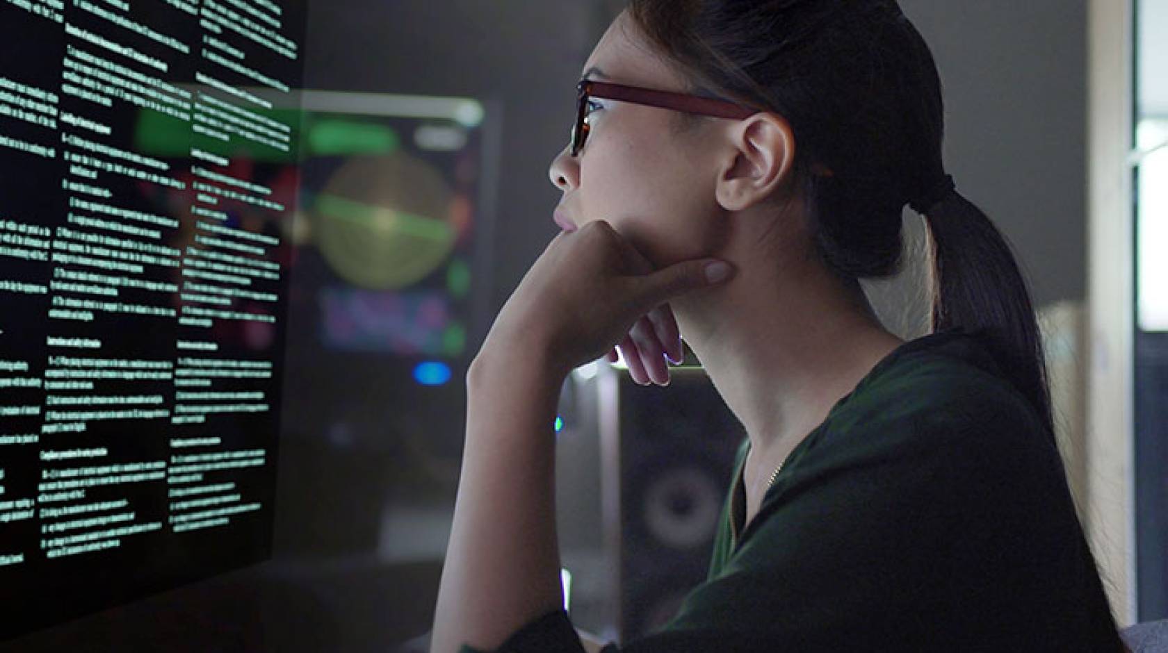 Young Asian woman looking at code on a screen in a dark room