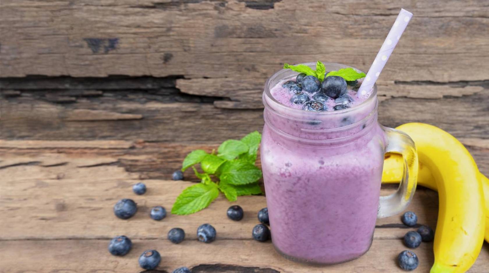 A purple smoothie with blueberries and a banana next to it on a table