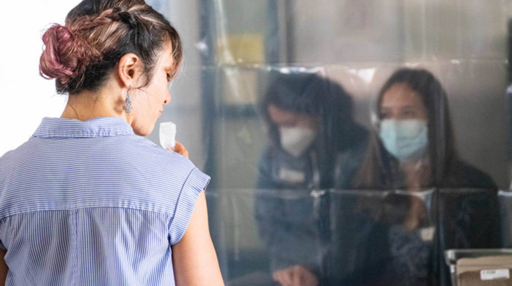 Woman staring through transparent plastic at people wearing PPE