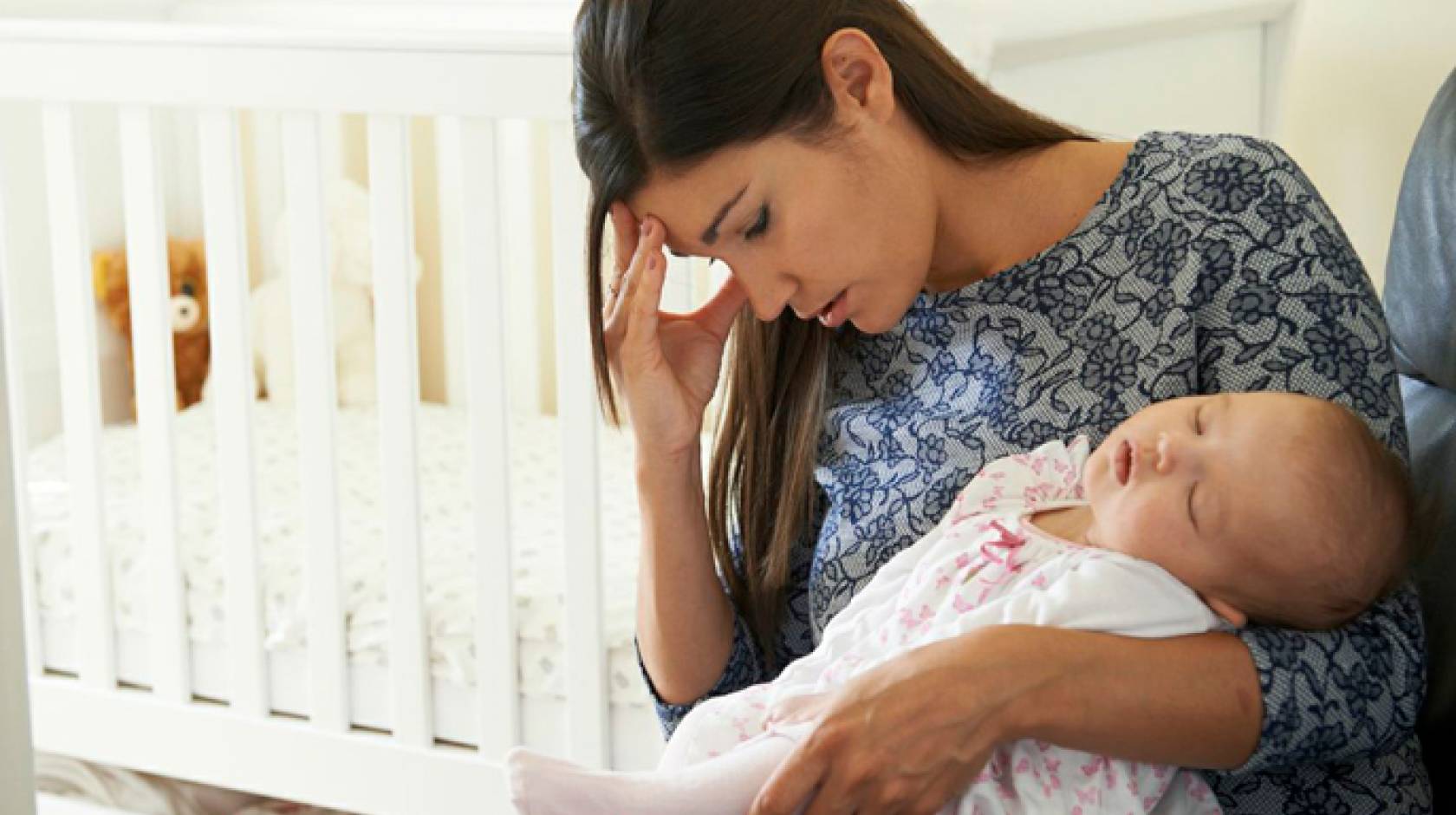 Young mom holds an infant with one hand and her head with the other hand