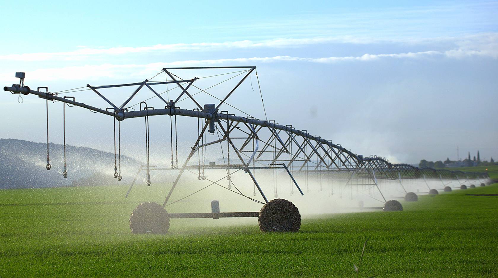 A spray irrigation system of metal irrigation equipment on a green field with mountains and clouds in the background