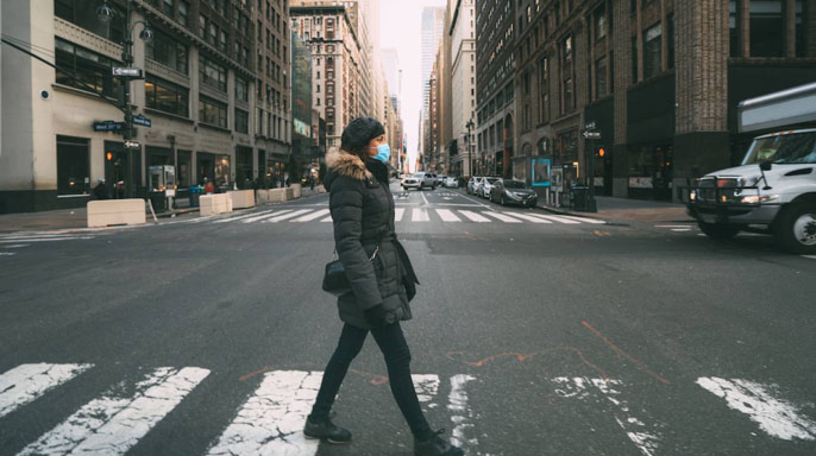 Woman walks down empty city street wearing a mask