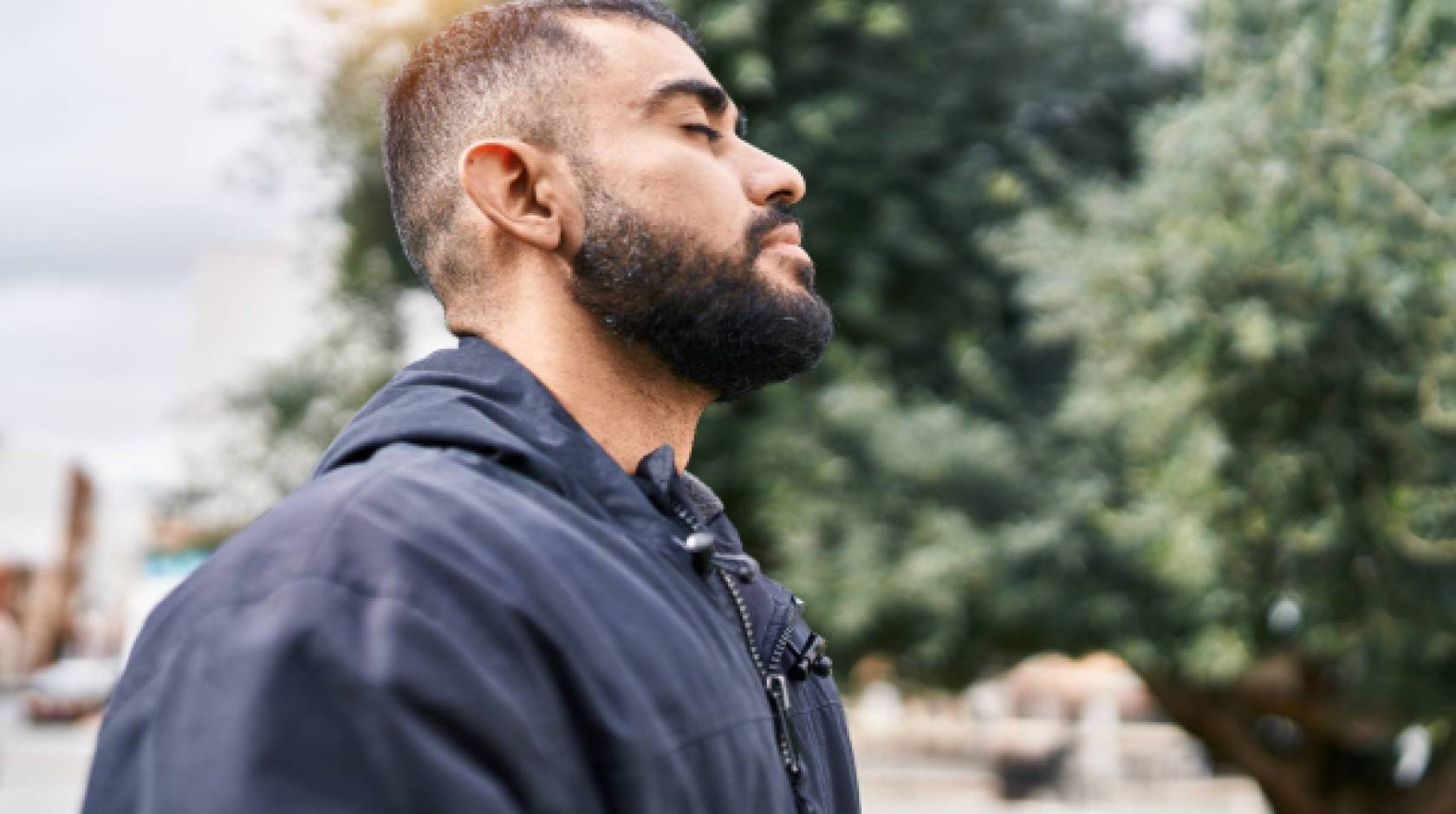 Young hispanic man with eyes closed taking a deep breath outside