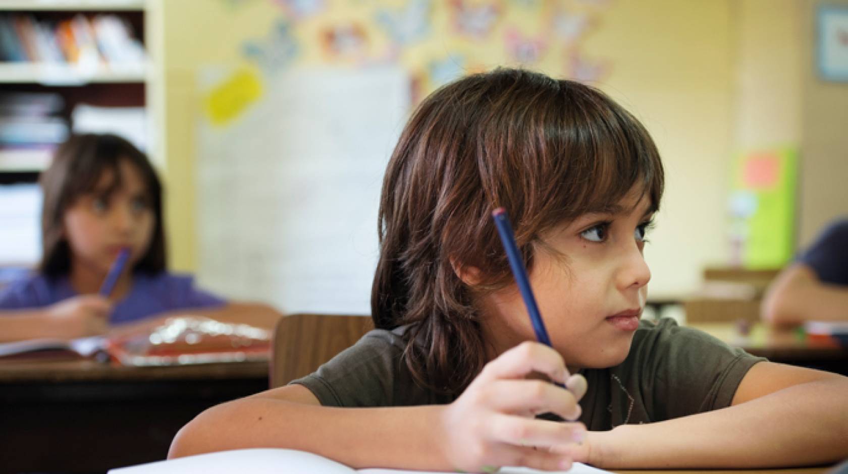 Boy looking up in a classroom, pencil in workbook