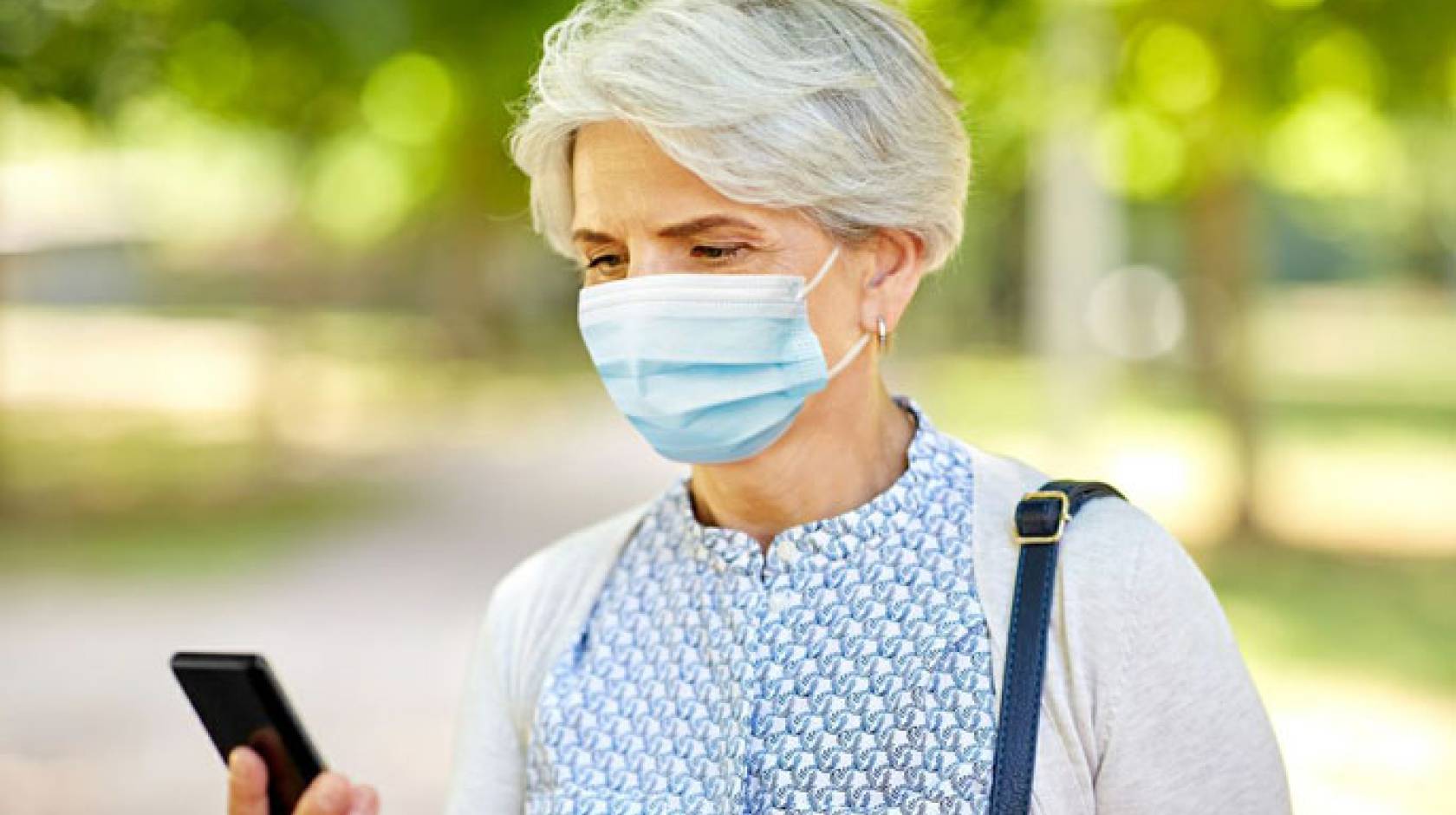 An older woman wearing a mask looks at her phone