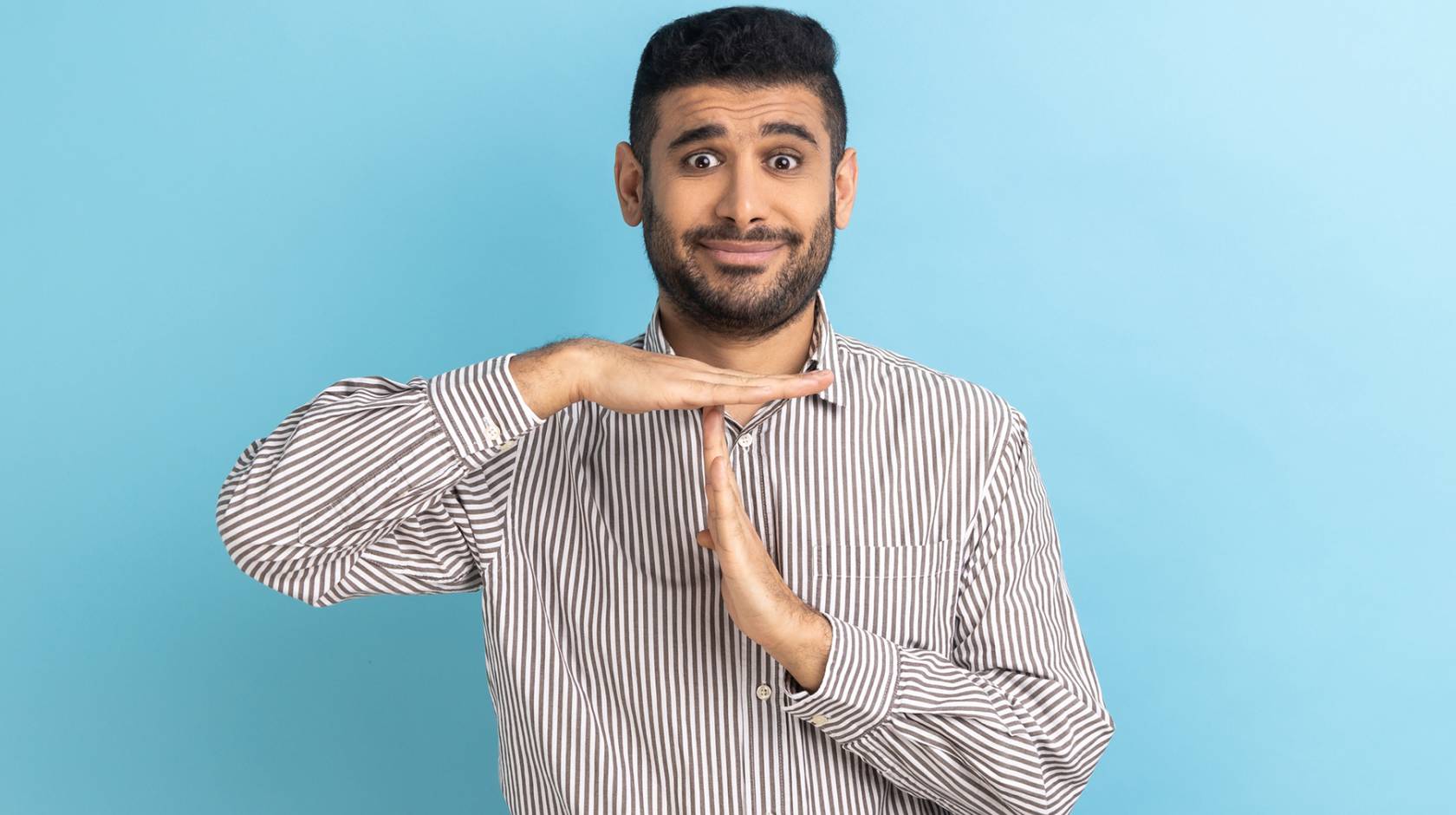 A bearded South Asian man making the timeout gesture