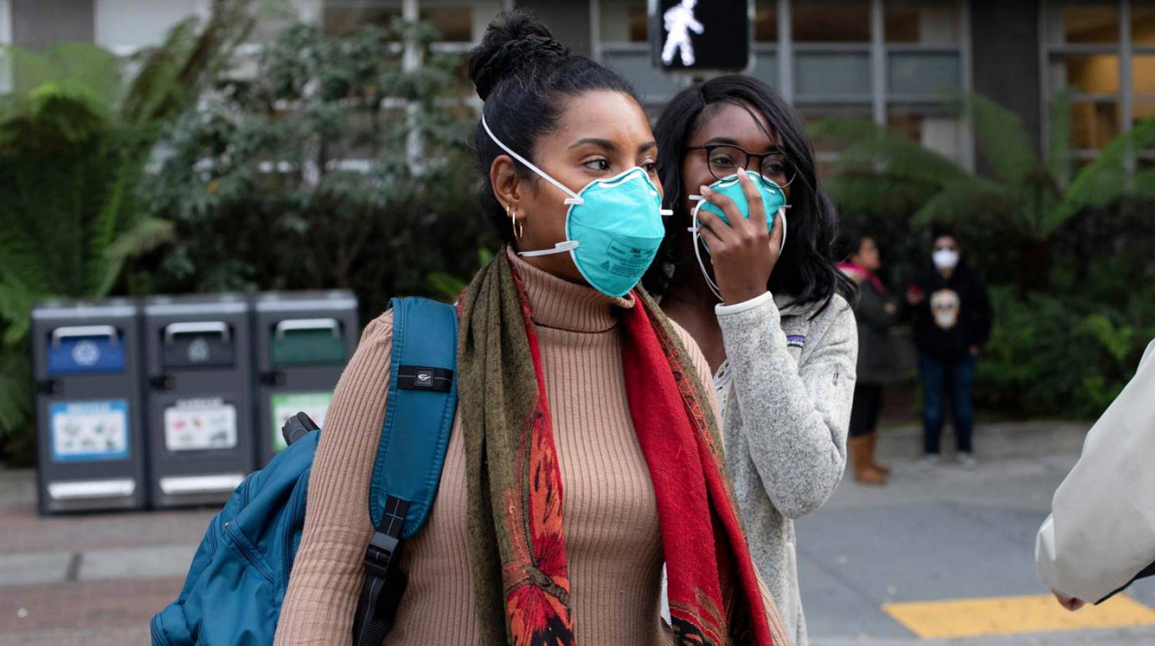 Two Black women wearing masks cross the street