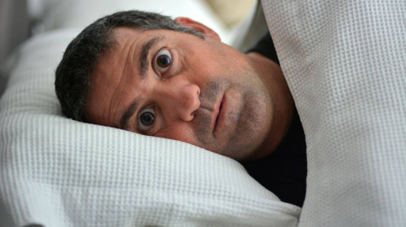 Man in bed looking surprised and scared