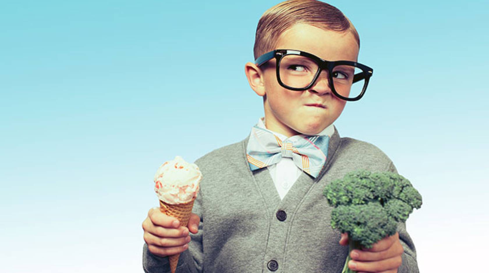 Mischievous boy holds ice cream and broccoli