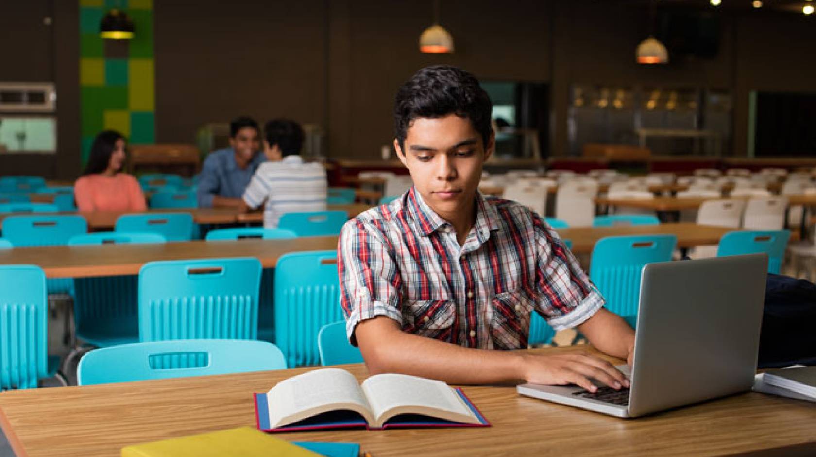 Male student typing on computer from book