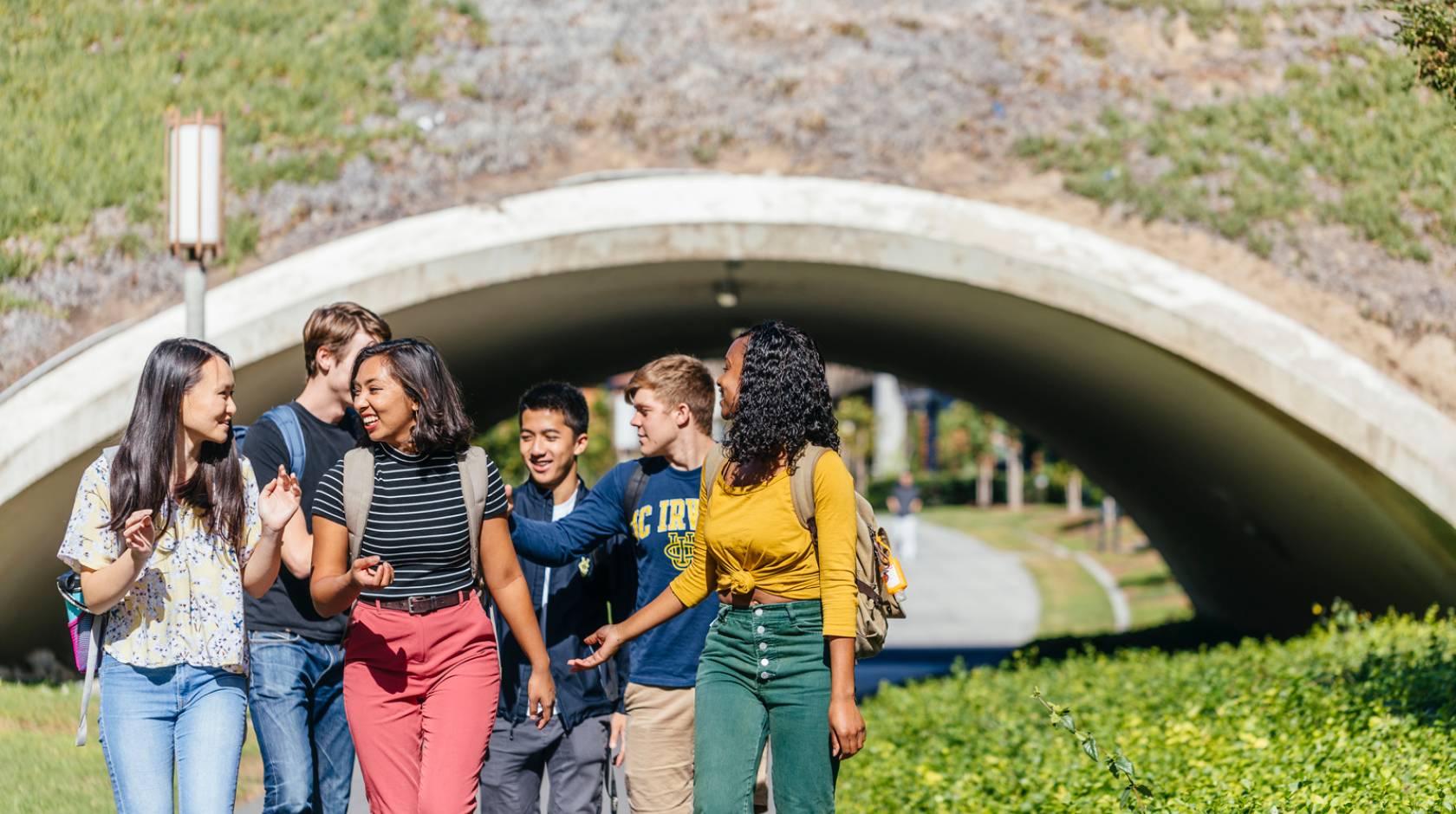 Diverse small group of happy students walking away from an arch on UC Irvine campus