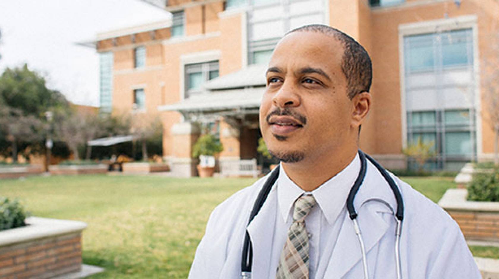 A Black professional stands in front of a brick office area