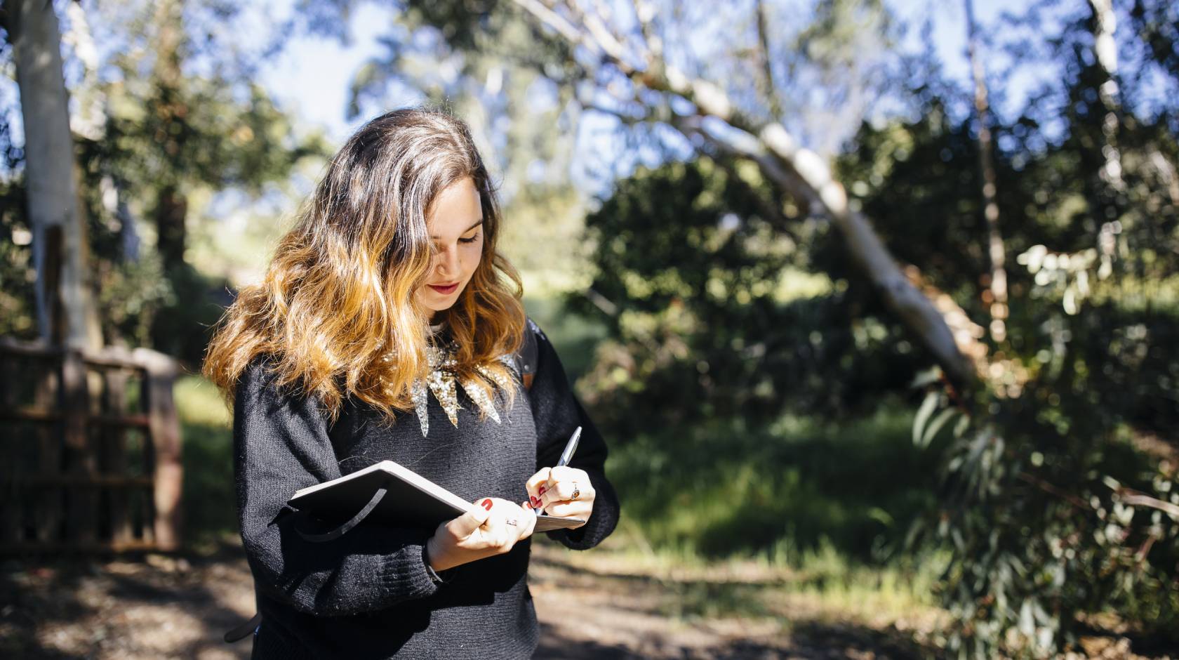 Young woman writing in notebook walking through woods