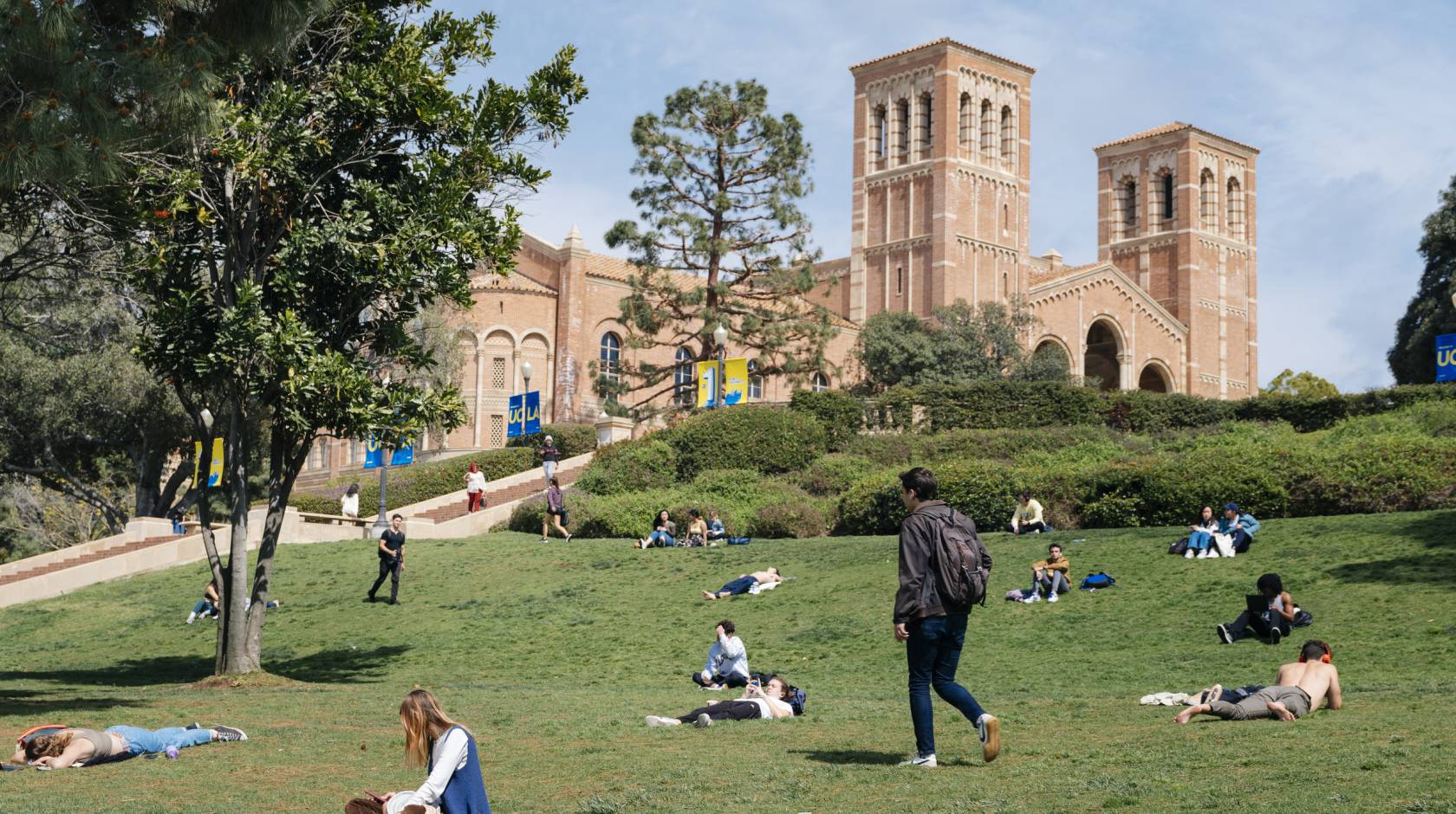 Students lounge and walk across the green on a sunny day at the UCLA campus; Royce Hall in the background