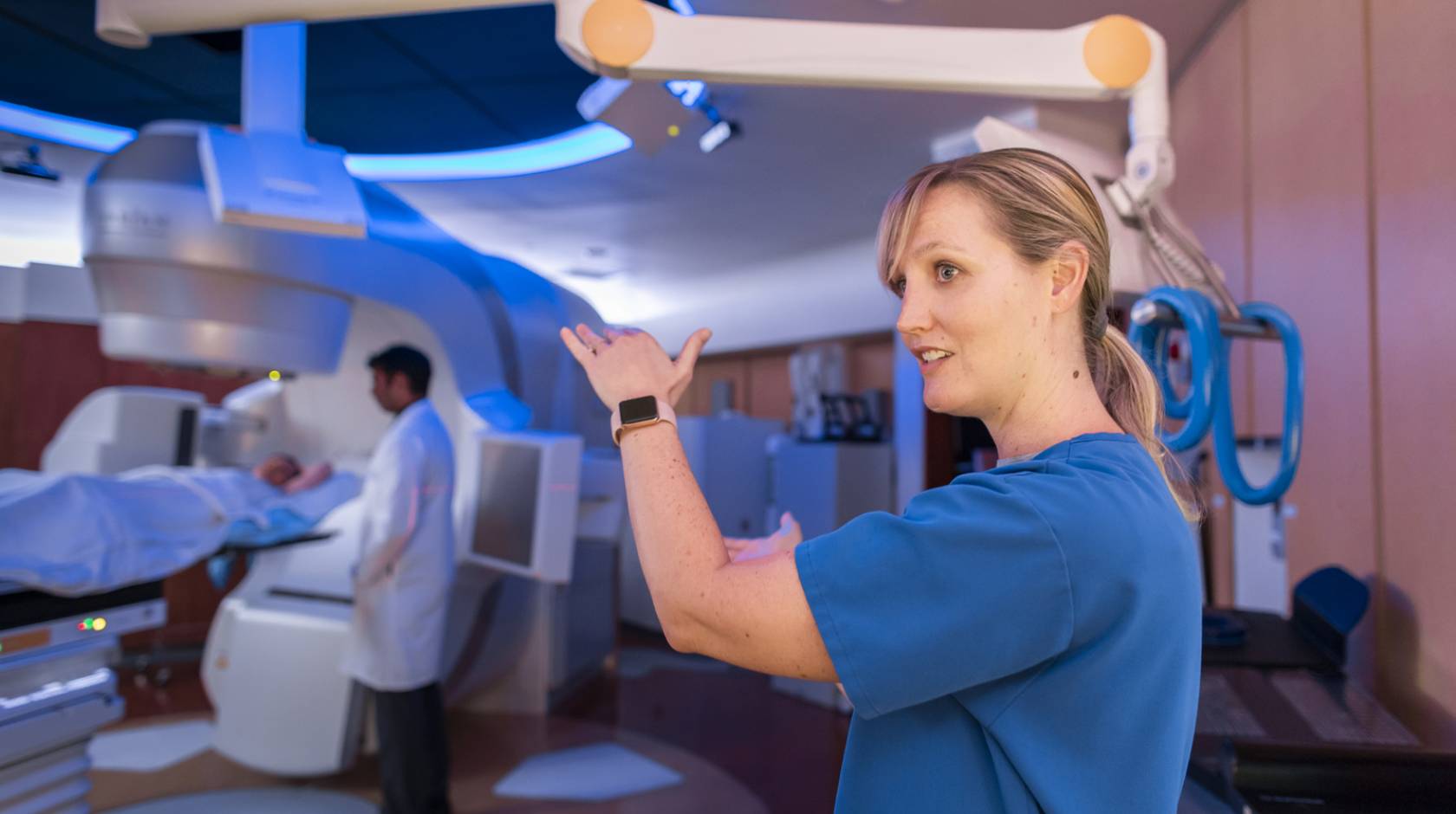 A nurse explaining something while a scan happens behind, doctor standing by