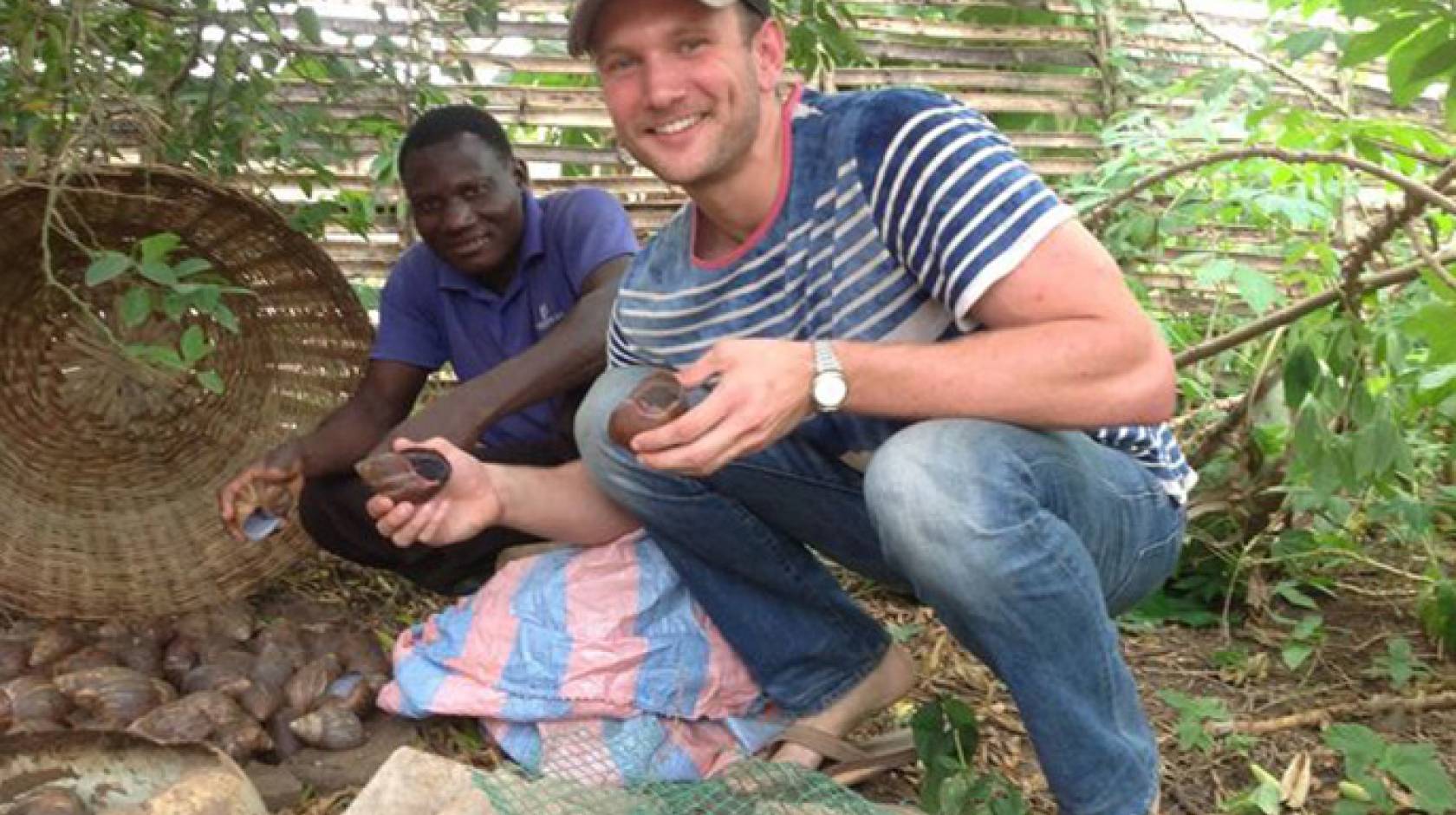UCLA senior Grant Guess (right) and farmer Thomas Bodzrenou hold giant land snails that will be bred, raised and sold to local markets and restaurants. The snails are the latest venture that Guess has launched to benefit a school for children with disabil