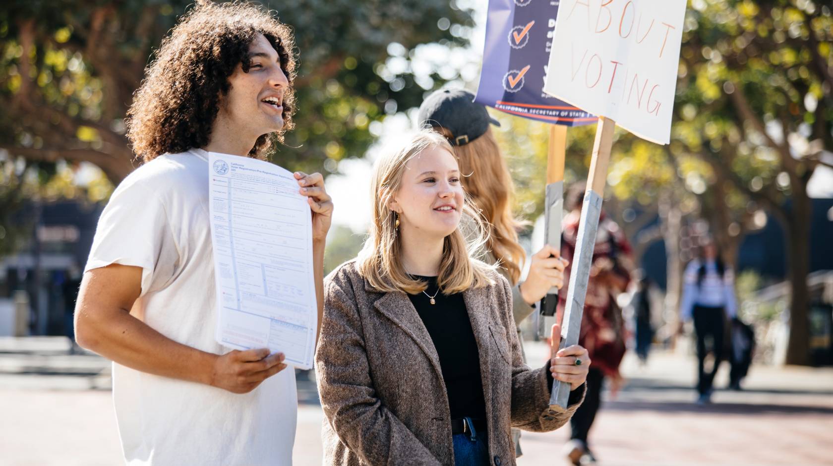 Alex Edgar and Skylar Betts hold up signs to encourage students to register to vote on the UC Berkeley campus