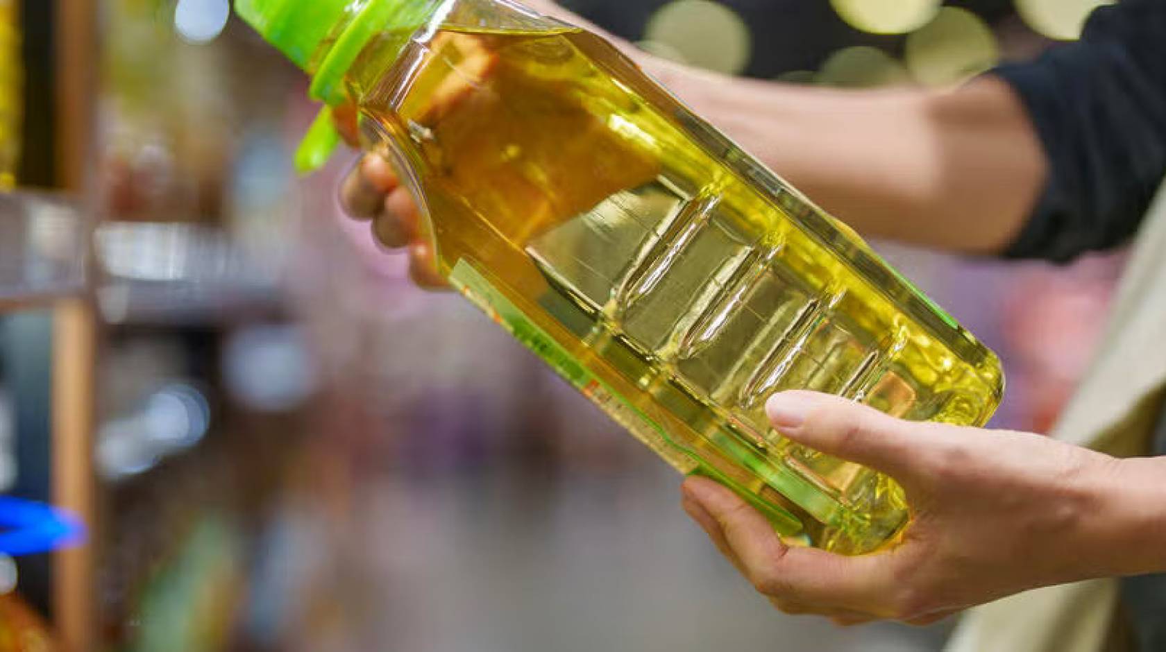 A pair of hands hold a bottle of soybean oil at an angle