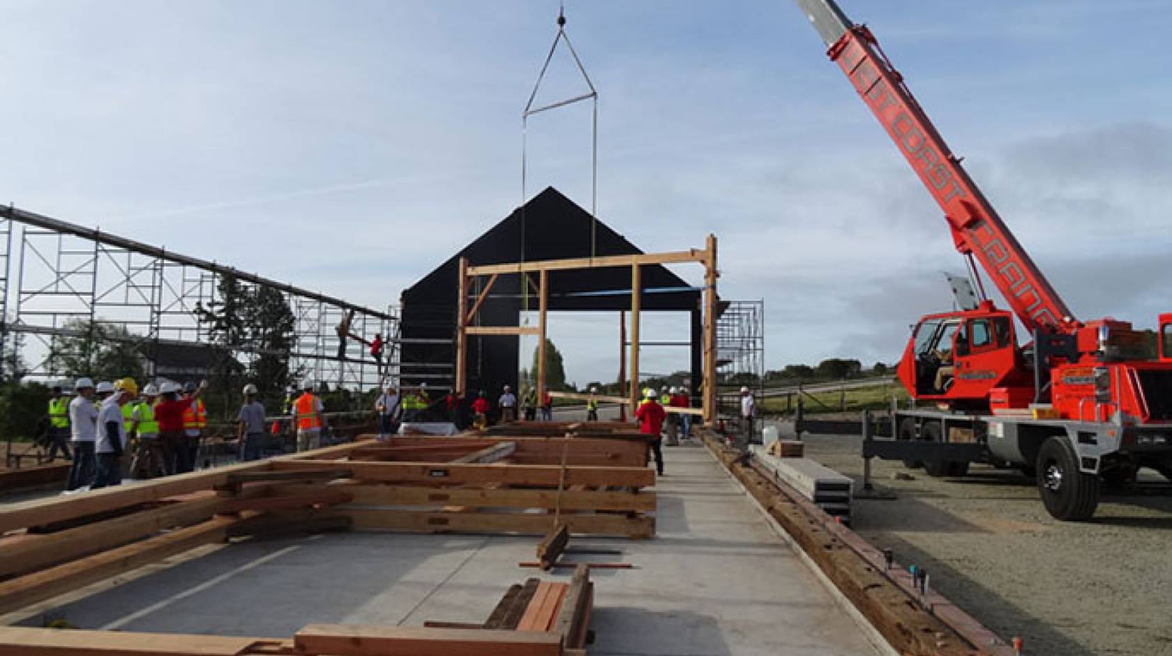 The first &quot;bent,&quot; a cross beam, posts, and supports joined by wooden pegs, is hoisted into place by a crane early Saturday morning while others, already assembled, await their turn on the new barn&#039;s concrete slab.