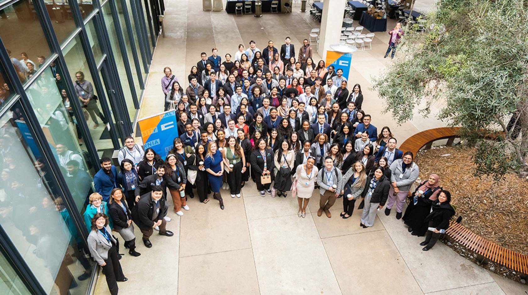 A group photo taken from above of ~200 young medical students in business attire, gathered in a courtyard.