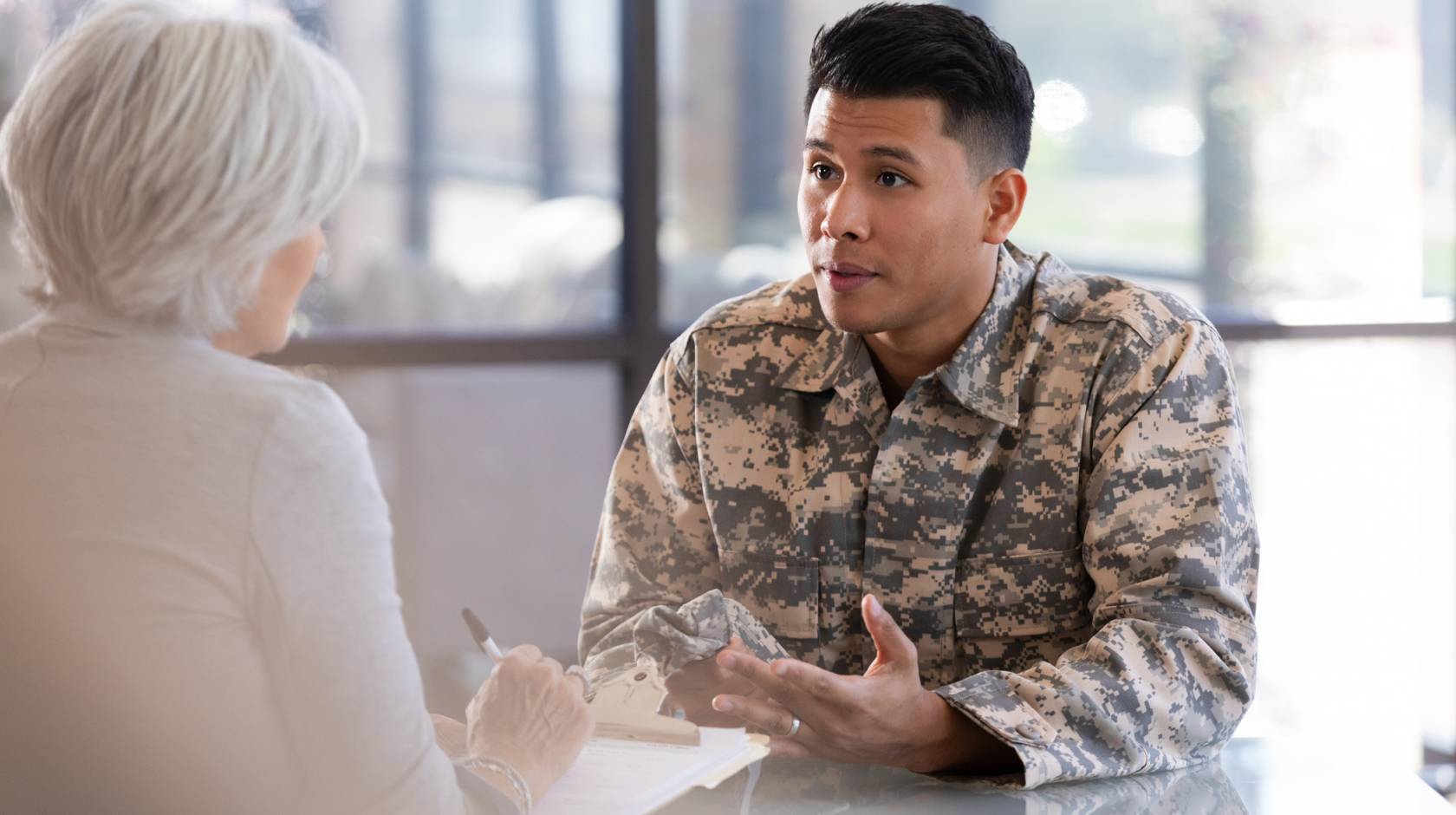 A soldier in uniform consults with a healthcare worker, discussing personal matters in a professional office