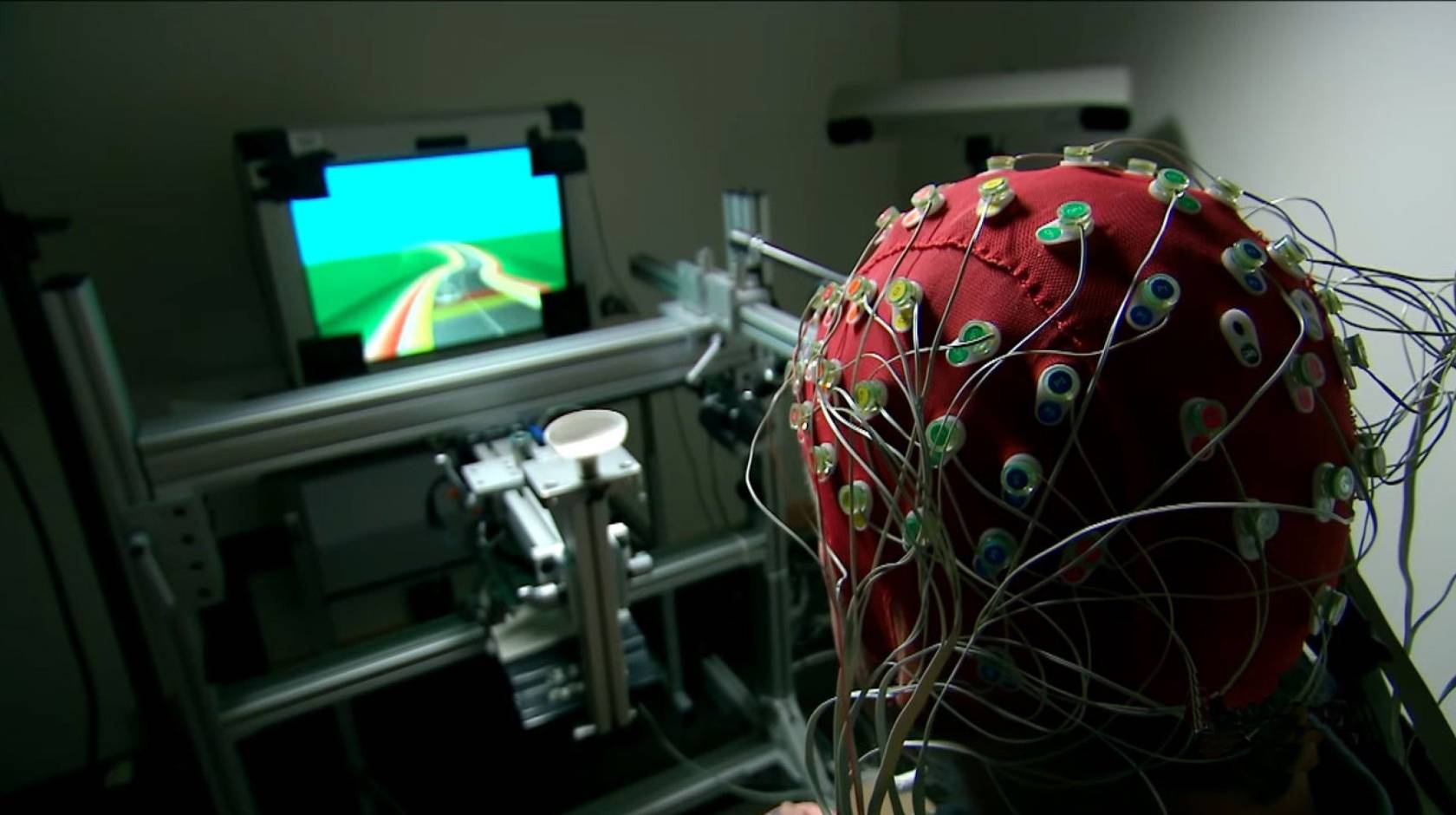 Someone with a cap for monitoring brain activity on their head plays a video game