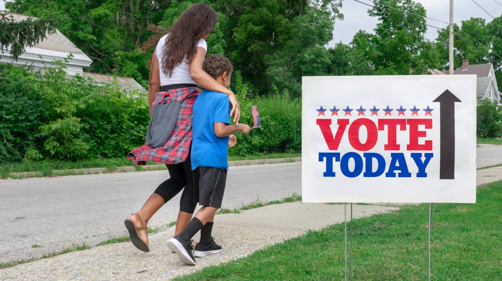 A Black woman and her son walk past a Vote Today sign to the polls