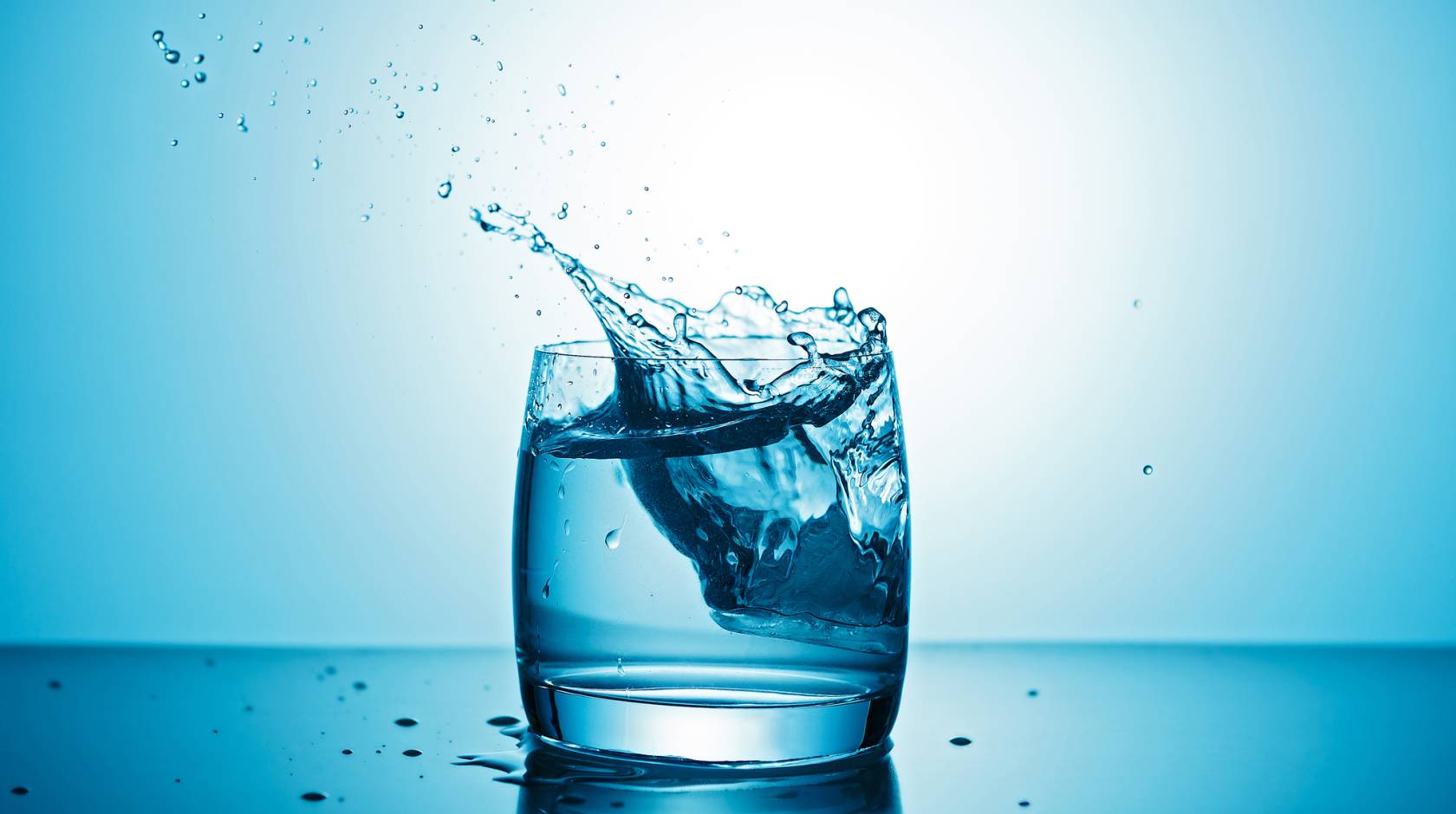 A glass of water with some water splashing out on a blue background